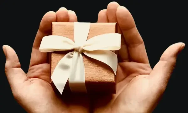 A hand holding a small gift box wrapped with a white ribbon and bow. Geat  vouchers at Ecape Rooms Drogheda