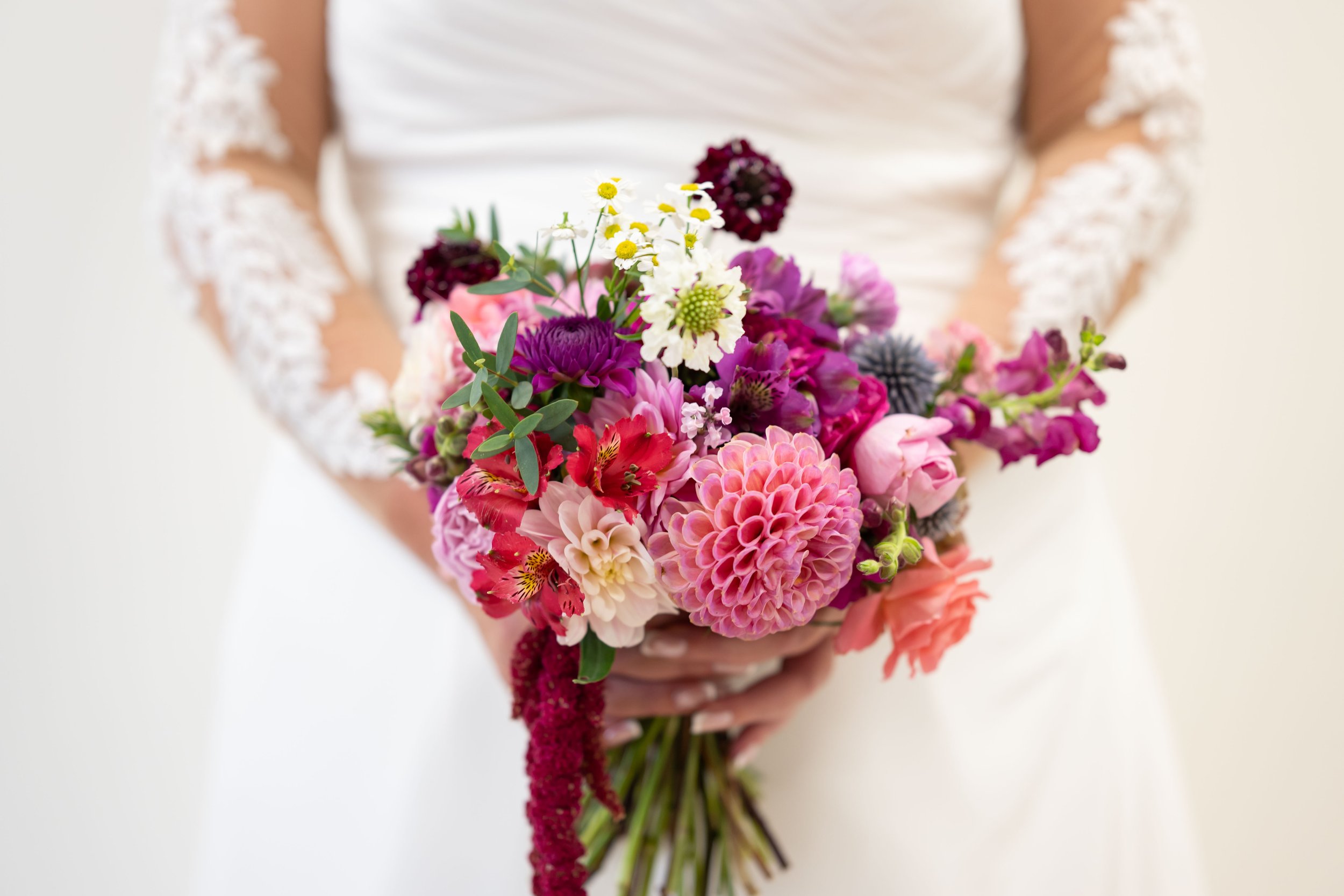 A person dressed in white holding a colorful bouquet of flowers with pink, purple, white, yellow, and dark red blooms.