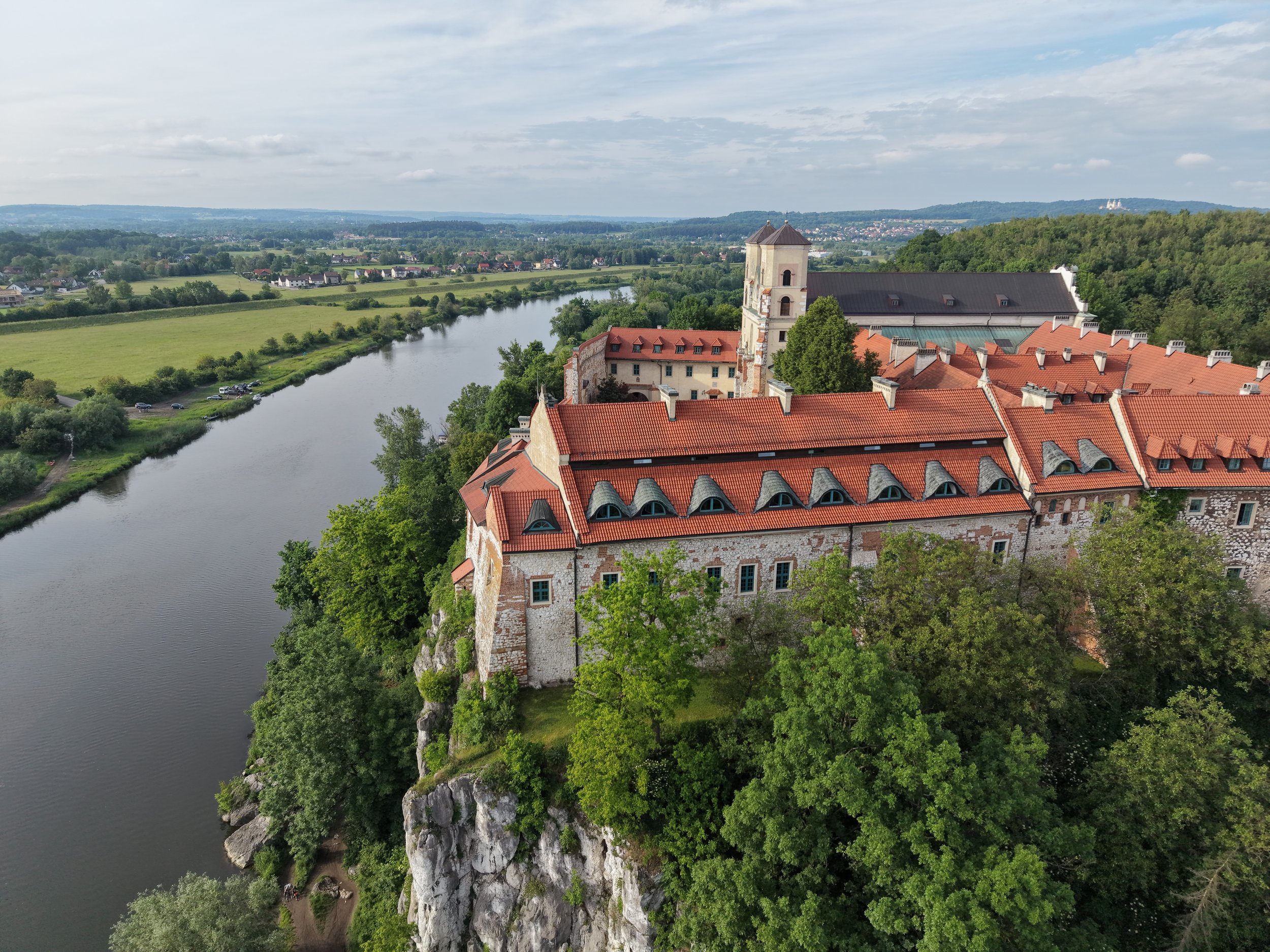 Drohnenaufnahme eines historischen Klosterkomplexes an einem Fluss mit Felswand und umliegender Landschaft