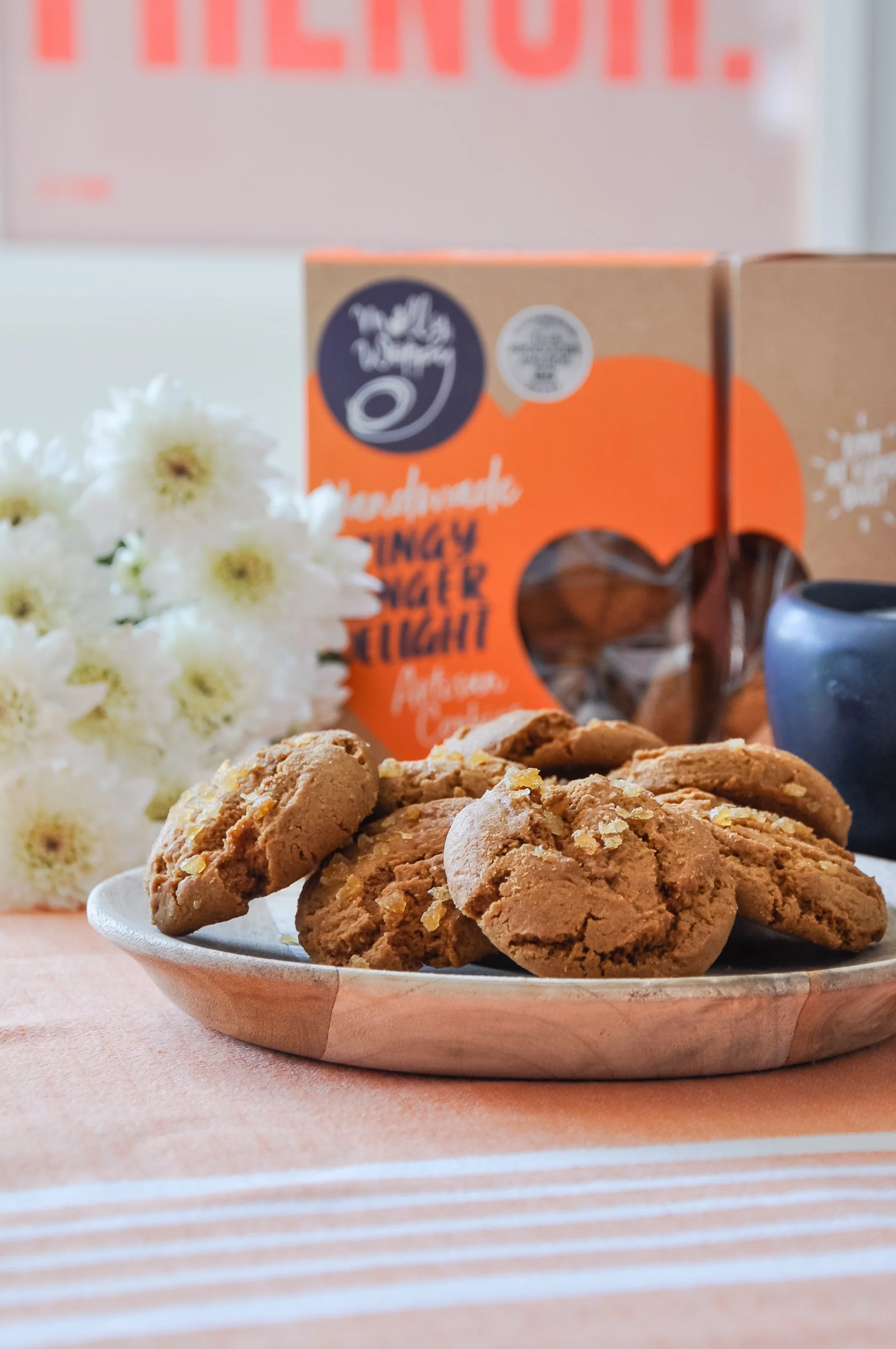 Plate of oatmeal cookies with white flowers and orange snack packaging in the background.