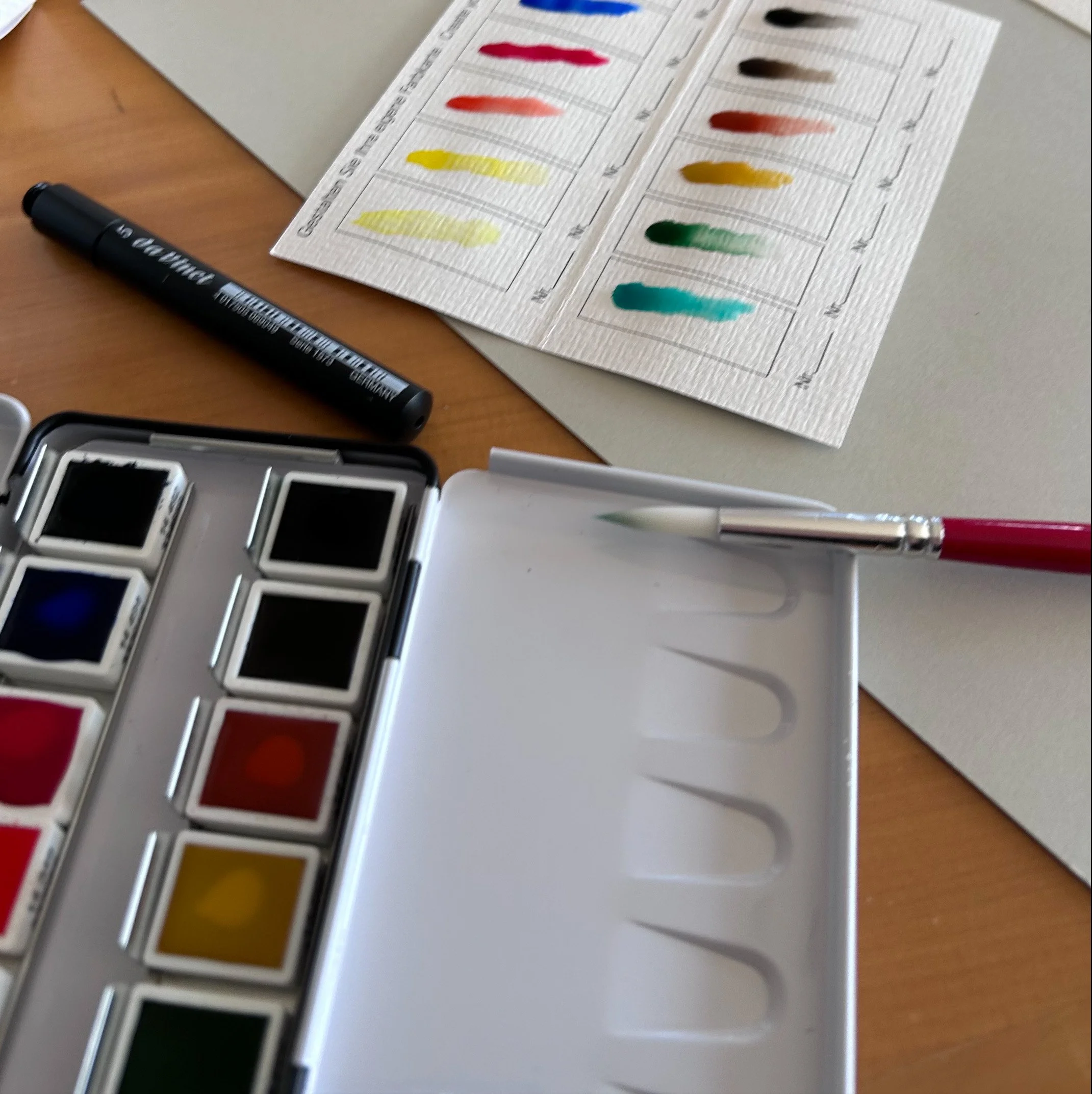 Color swatch chart with various shades organized in rows on white paper, placed on a wooden surface with a black marker nearby.
