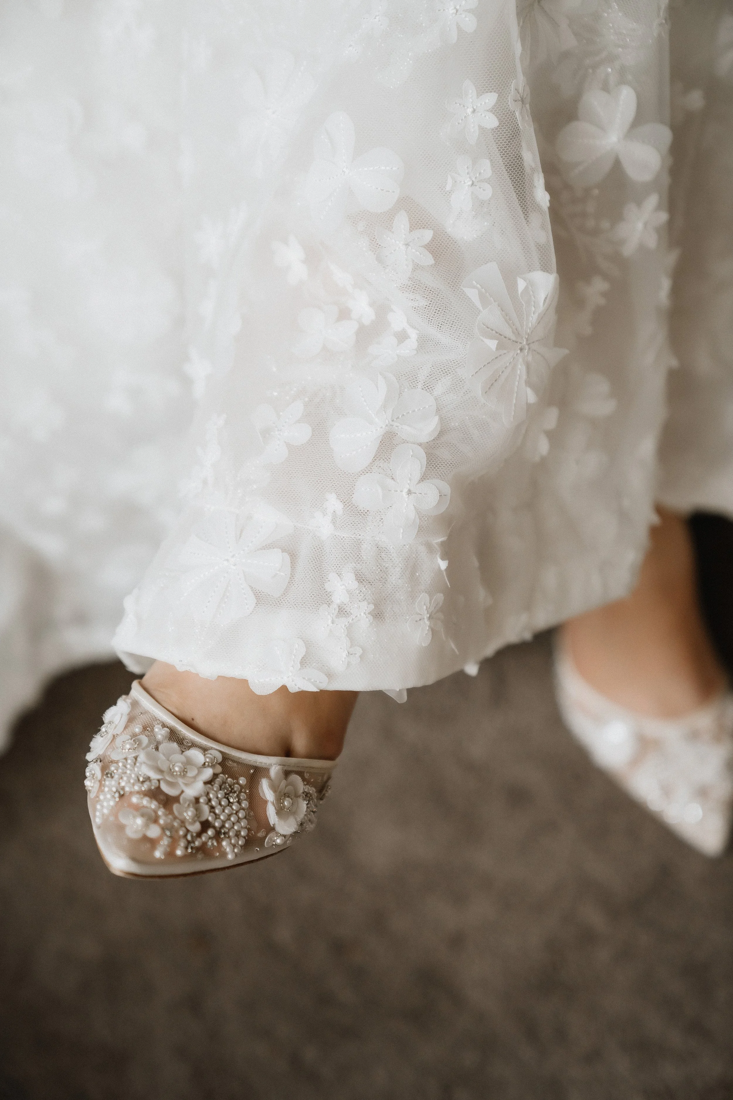 Close-up of a little girl's foot wearing a dress shoe with floral embellishments and a satin dress with lace and floral embroidery.