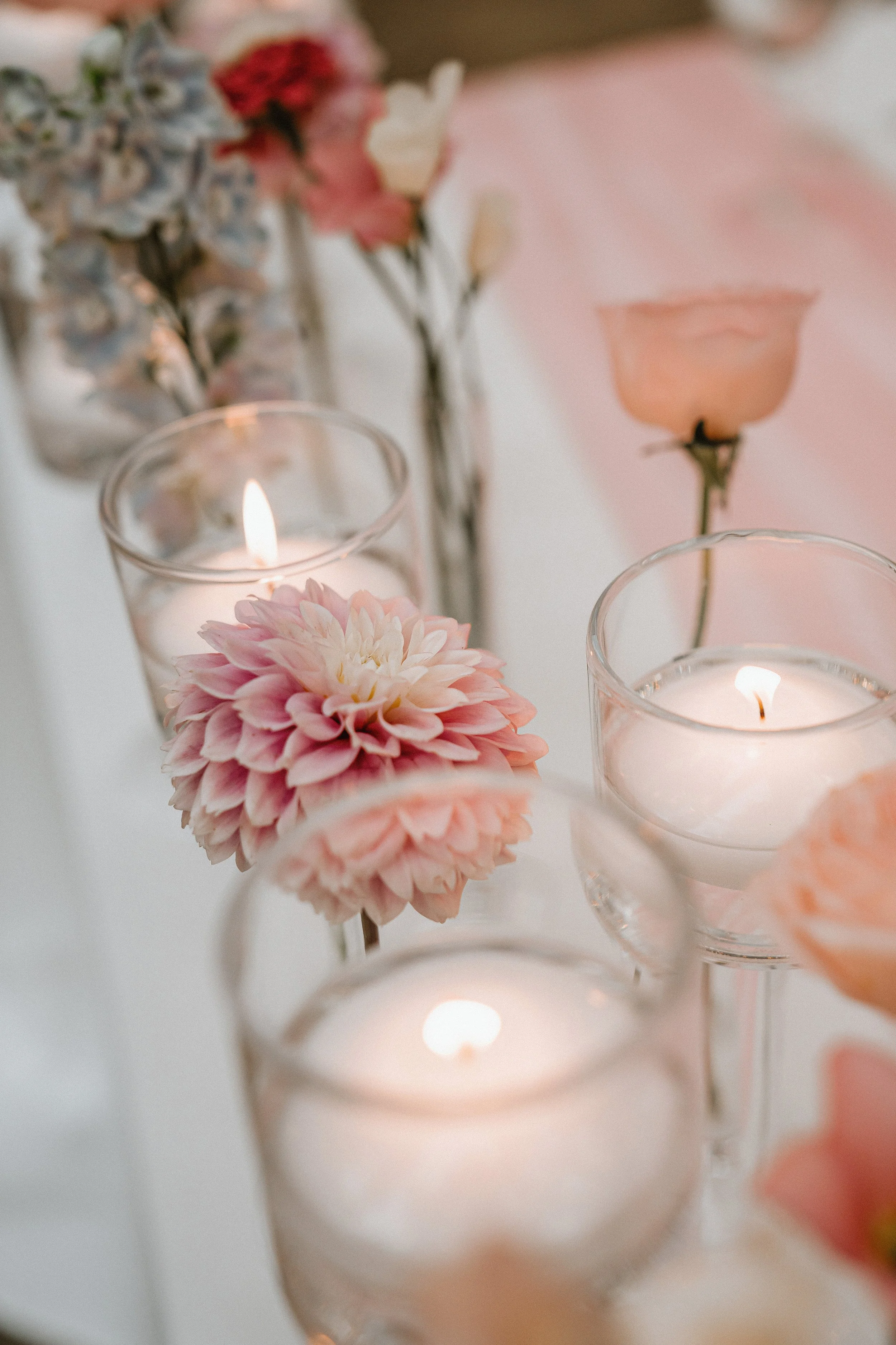 Pink flower in a glass vase with a candle in the background