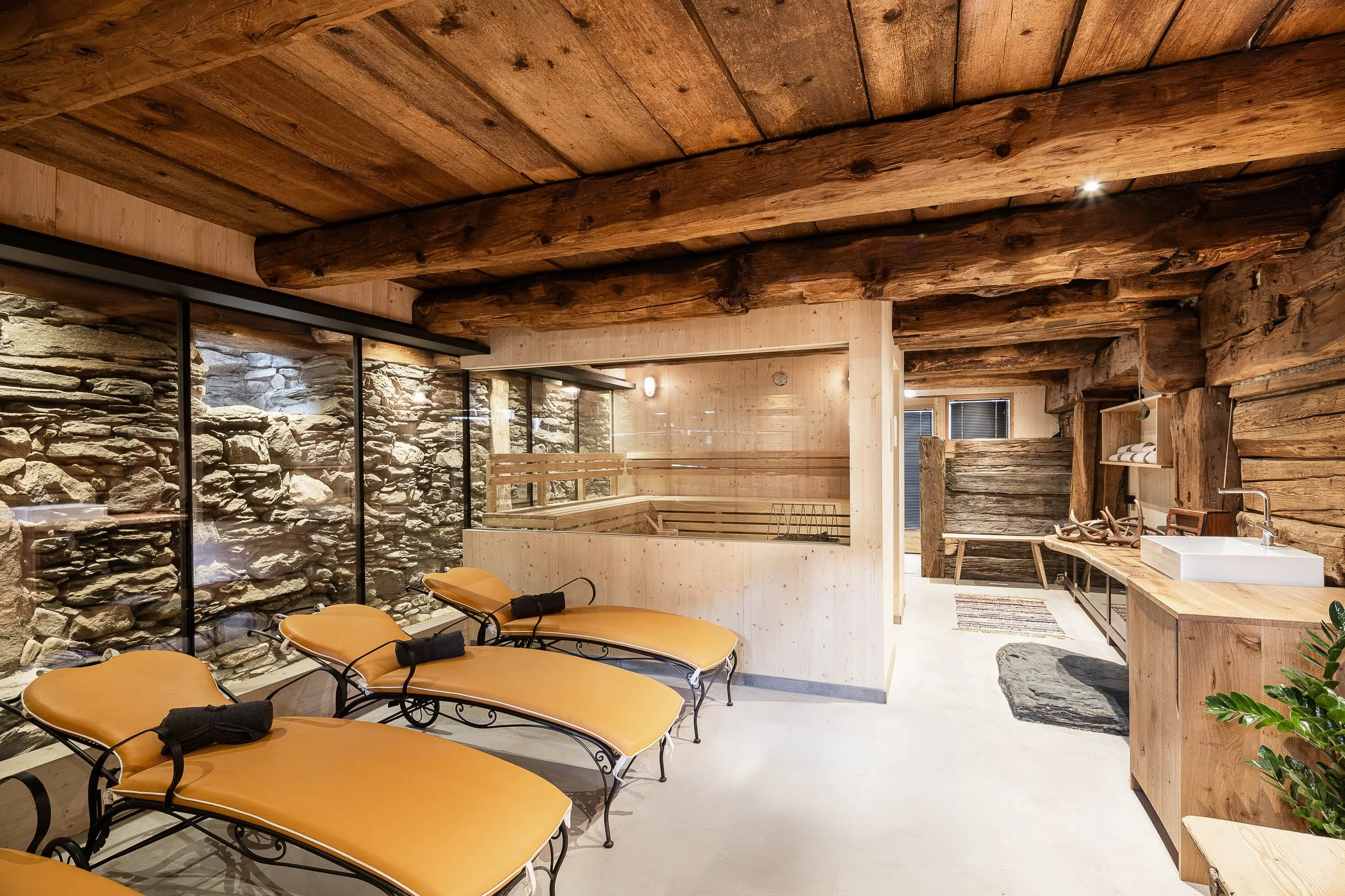 Innenraum eines Spa- oder Wellnessbereichs mit Holzdecke, Steinwand, Liegen und einer Waschküche.