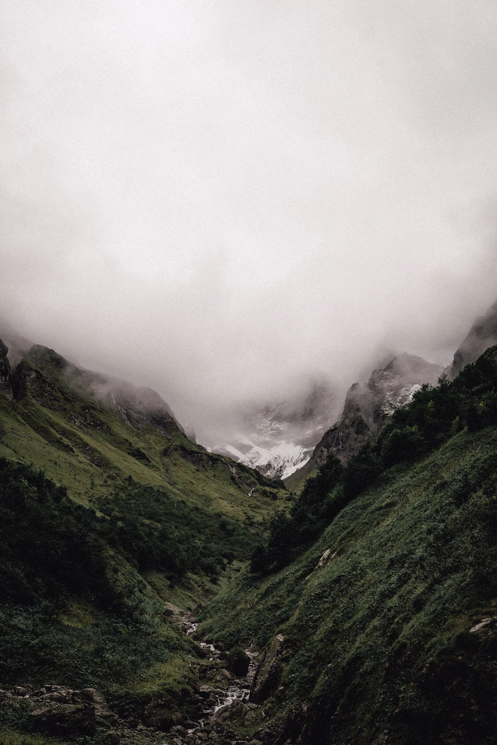 Bergtal mit Fluss, grüne Hänge, Nebel und Berge im Hintergrund