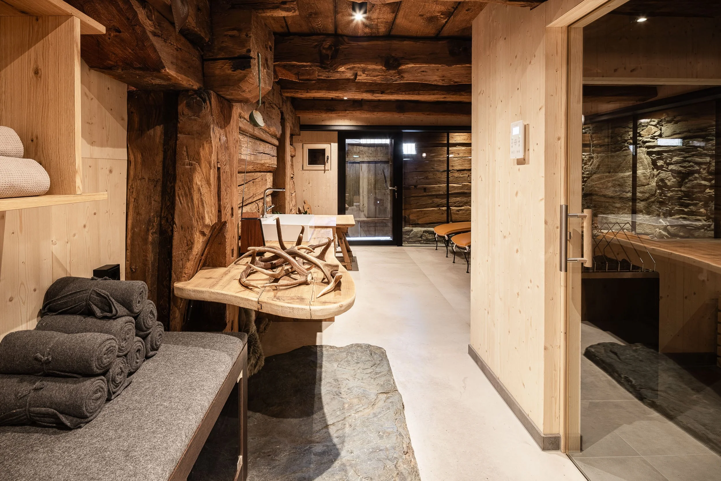 Innenansicht eines rustikalen Wellness- oder Spa-Bereichs mit Holzdekor, Steinelementen und Wellnessliegen.