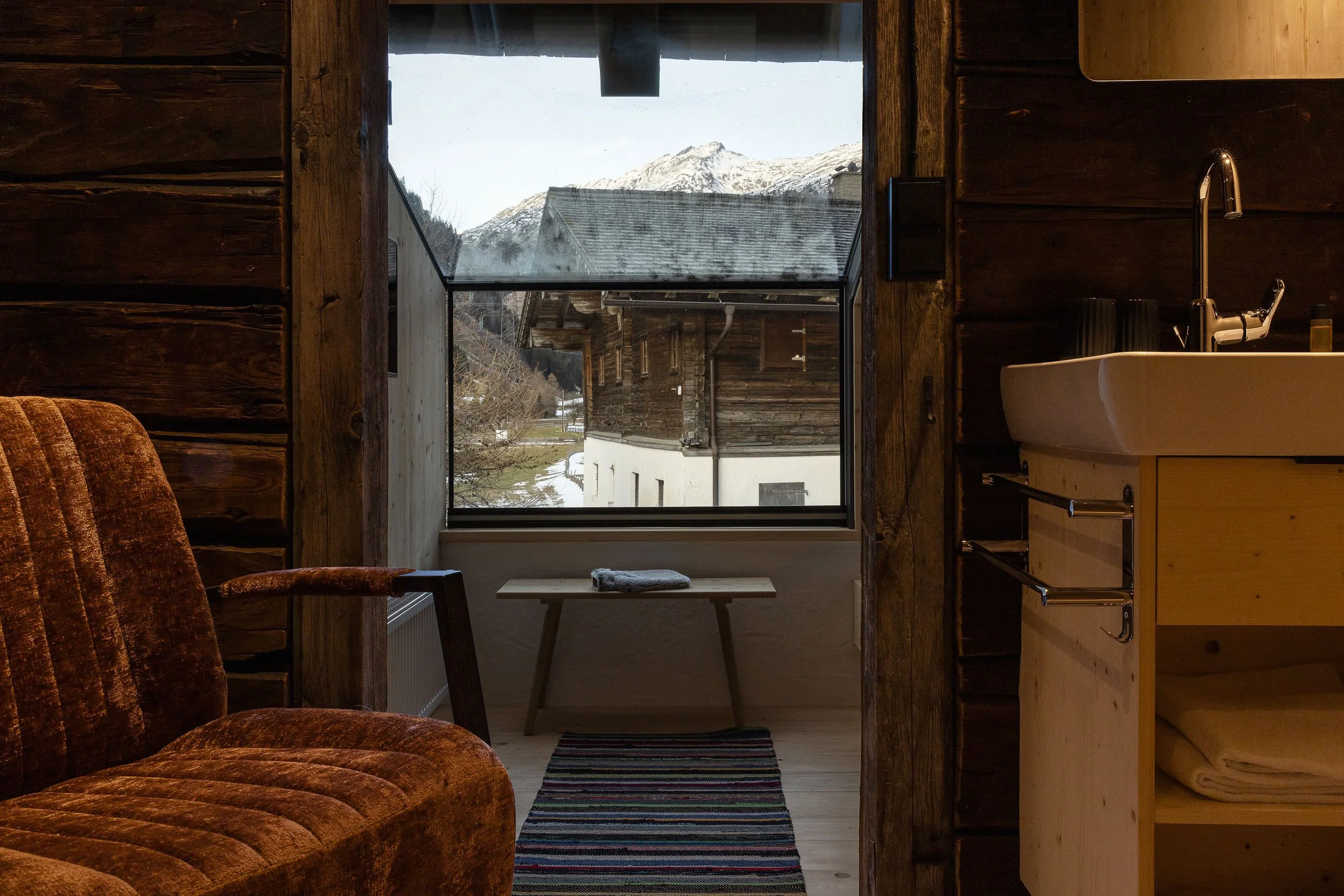 Blick aus einem Fenster auf verschneite Berge und traditionelle Holzhäuser im Tal