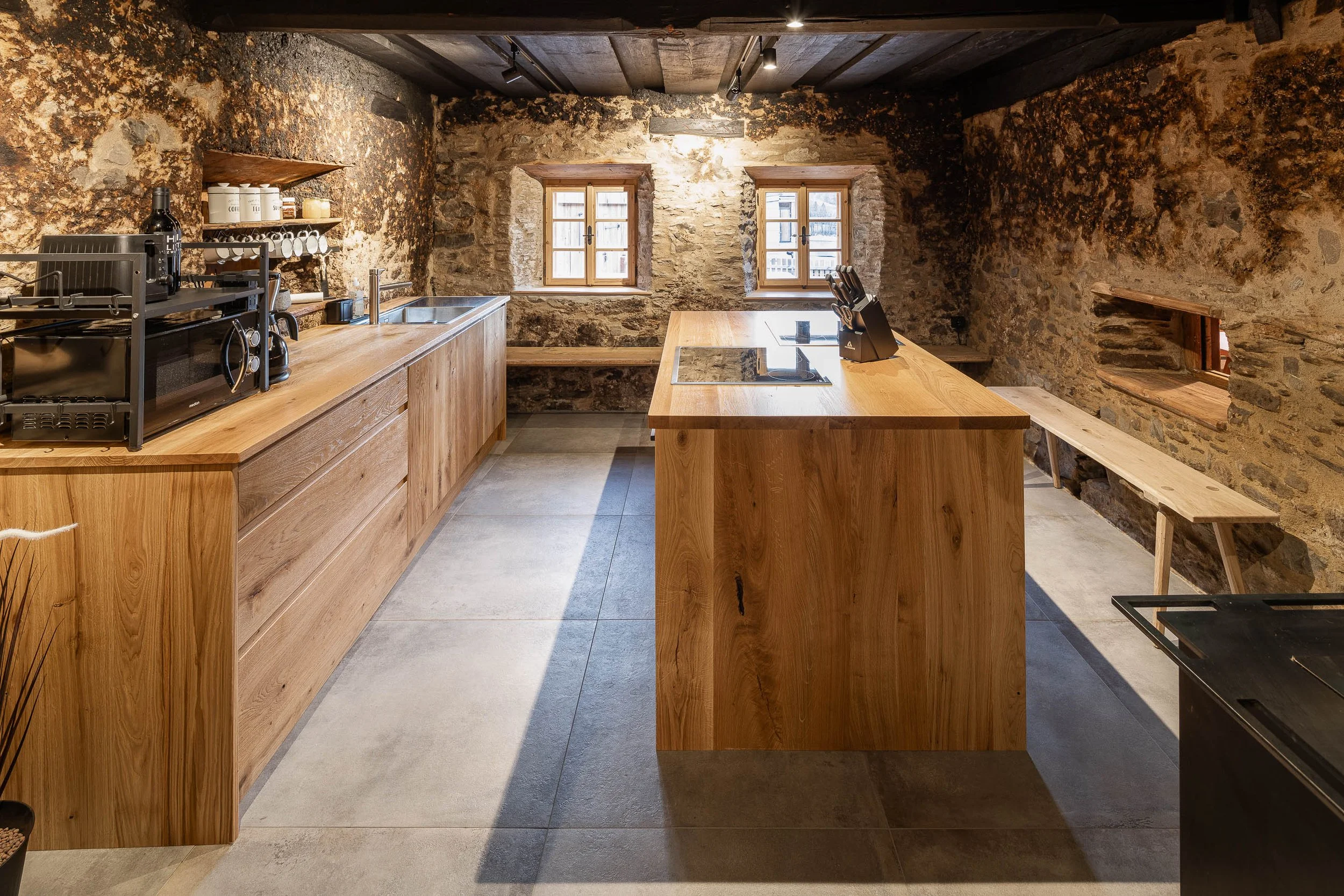 Küche mit rustikalen Steiwänden, Holzmöbeln und zwei kleinen Fenstern