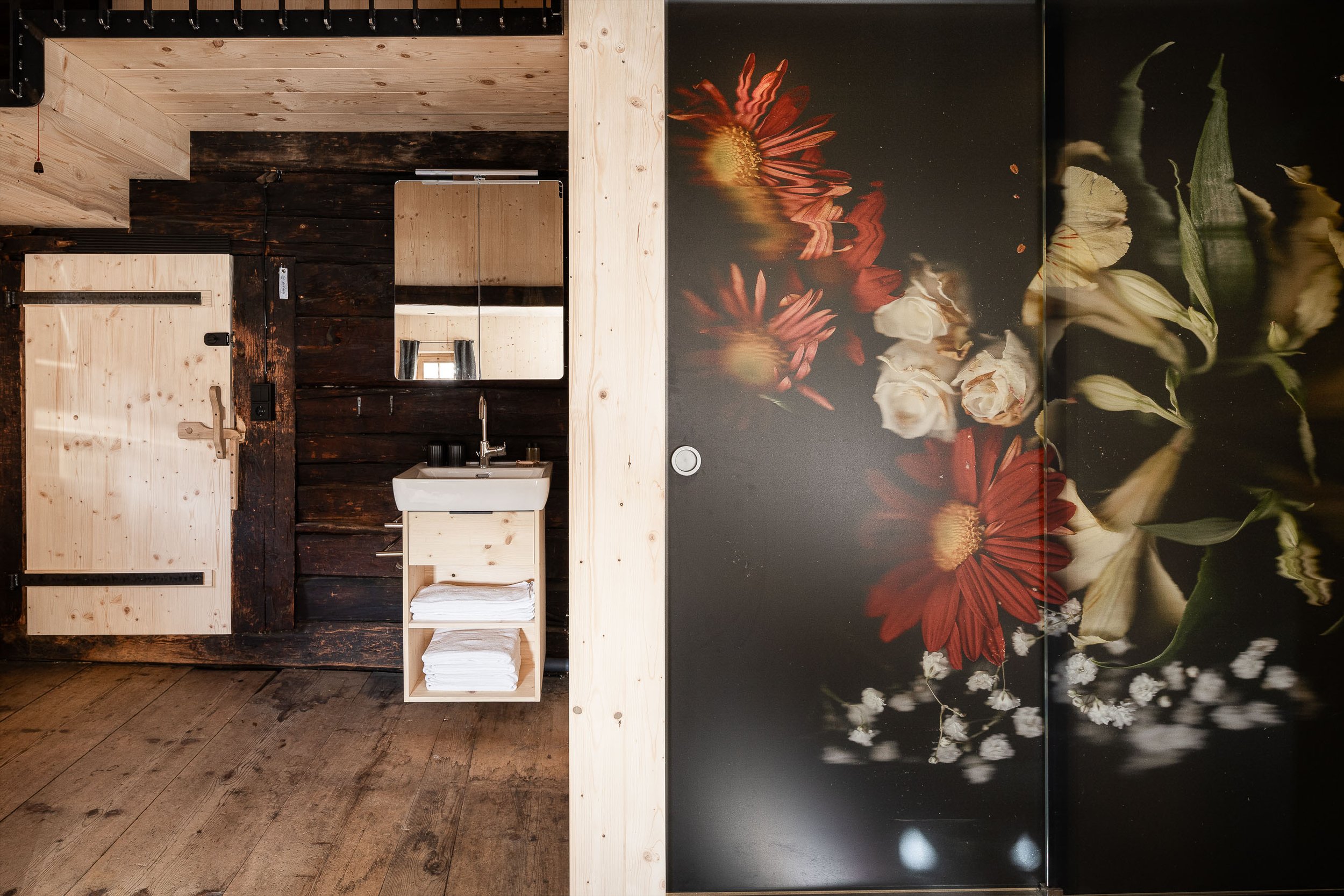 Rustikale Holz- und dunkle Blumenwand mit handgemachtem Waschbecken in einem Spa oder Badezimmer, darunter Handtücher.