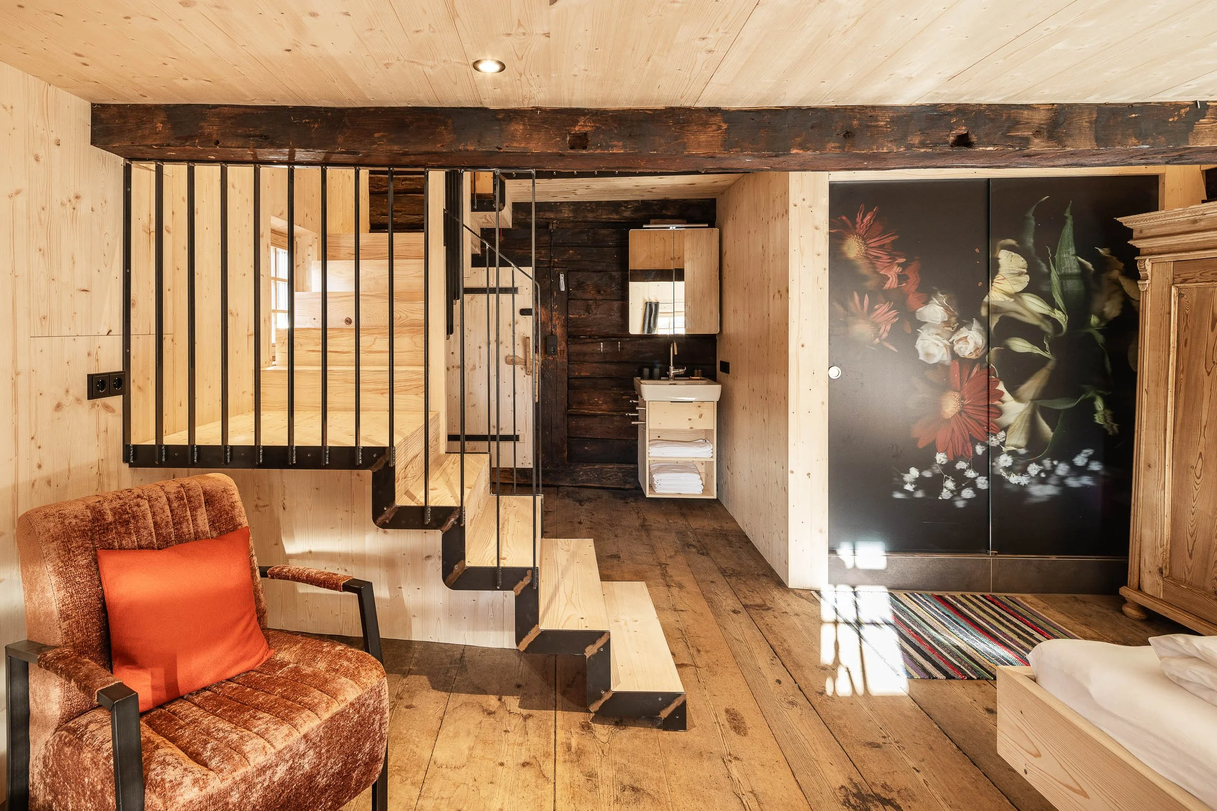Innenraum eines rustikalen Hauses mit Holzdecke, Treppe, Spiegel, Sofa und Wand mit Blumendekor.