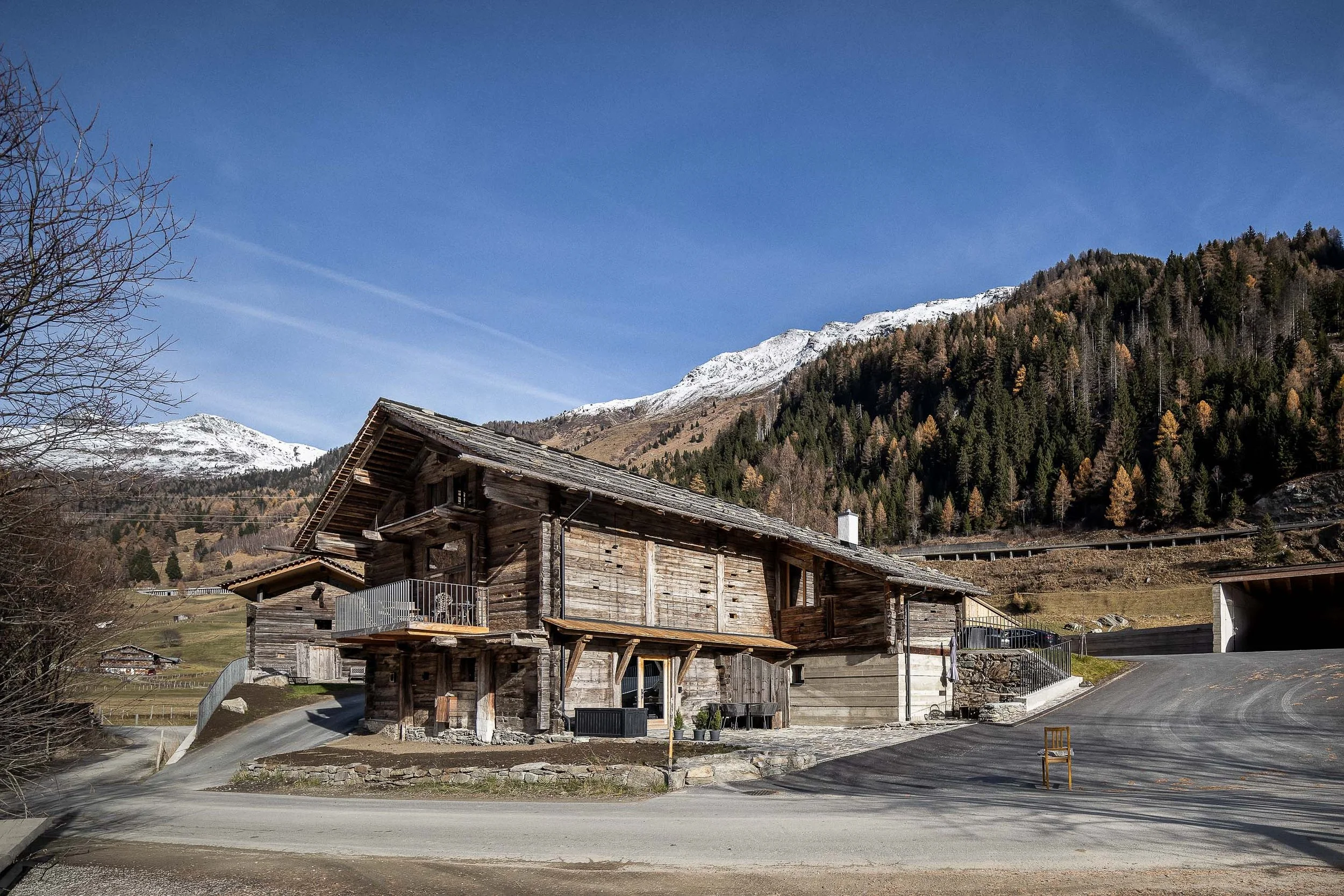 Altes Holzhaus in einer alpinen Bergregion, umgeben von Snowcapped Mountains, unter klarem blauen Himmel.