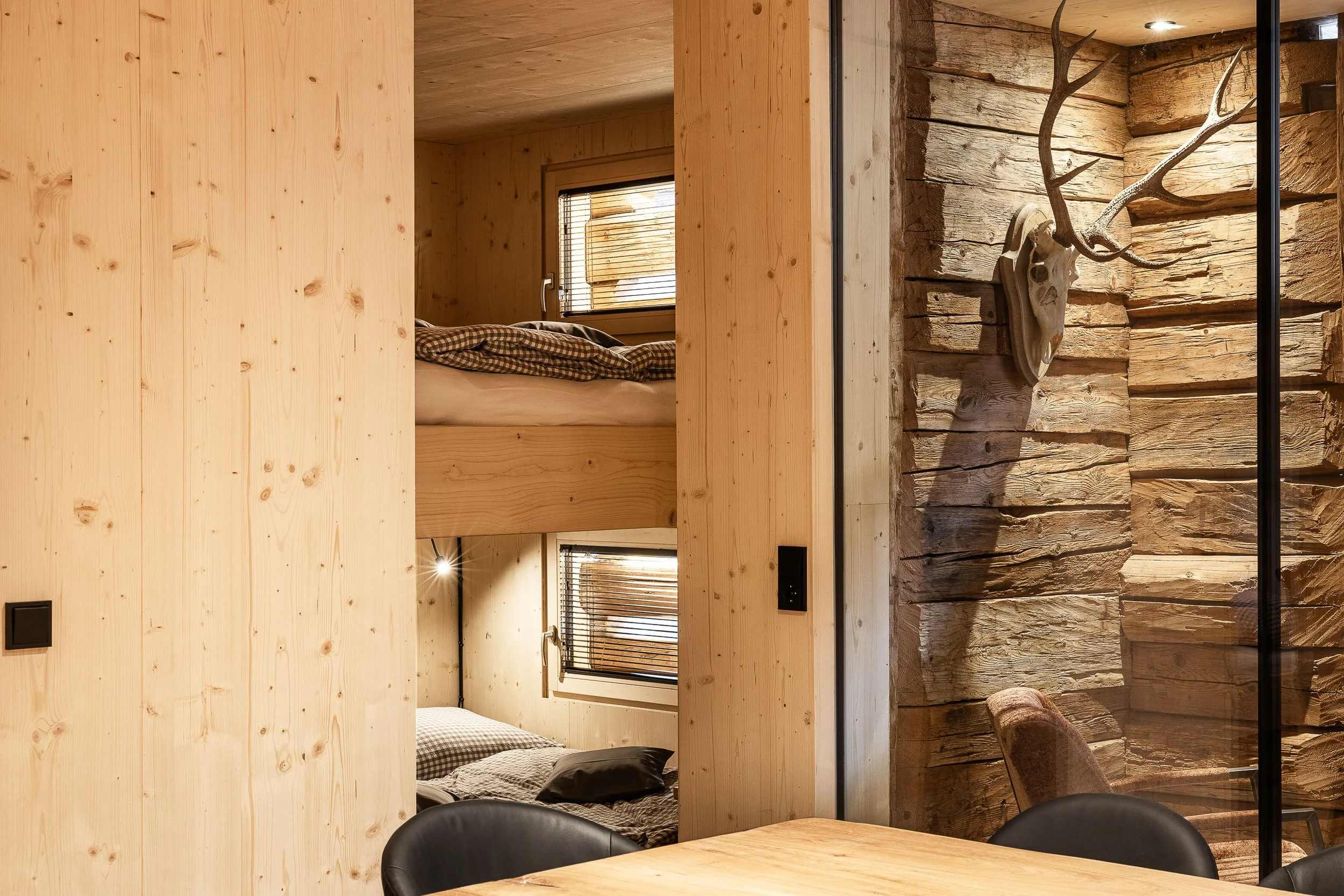 Innenraum eines Holzhauses mit einem Schlafzimmer im Hintergrund, einer Tierpräparat-Hirschgeweih an der Wand und Holzmöbeln im modernen rustikalen Stil.