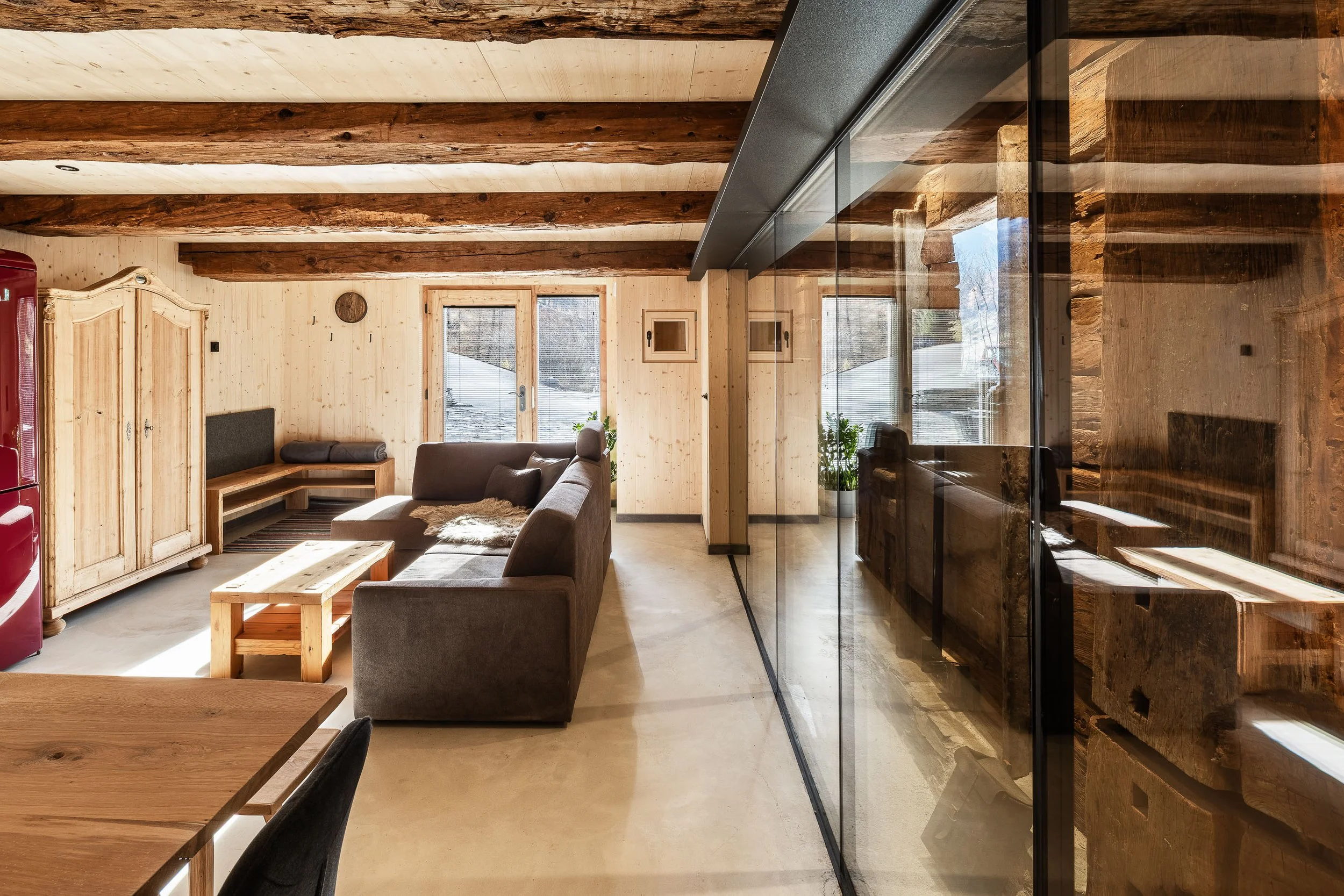 Innenaufnahme eines modernen Wohnzimmers mit Holzbalkendecke, großen Fenstern, Sofa, Couchtisch und Holzregal.