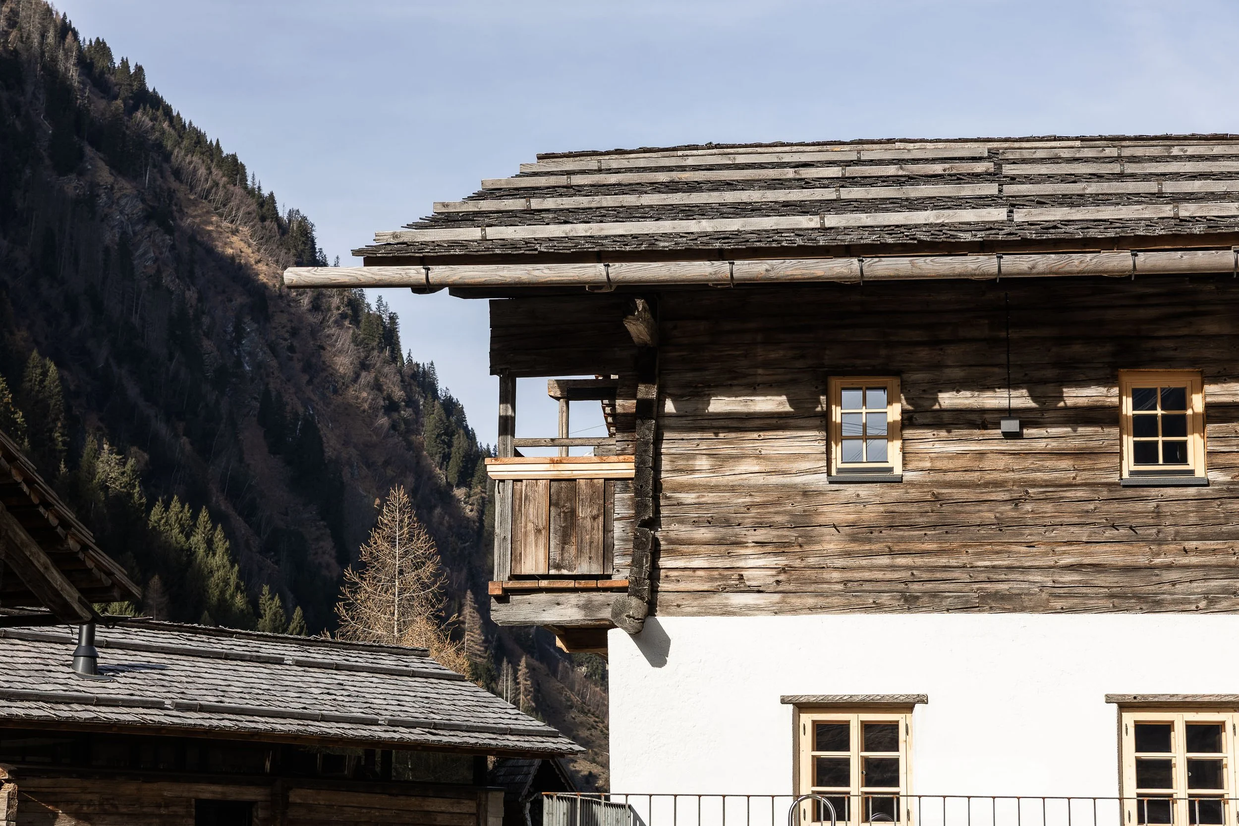 Ein Haus mit Holz- und Putzfassade vor einem Berg im Hintergrund, mit kleinen Fenster und Terrasse.