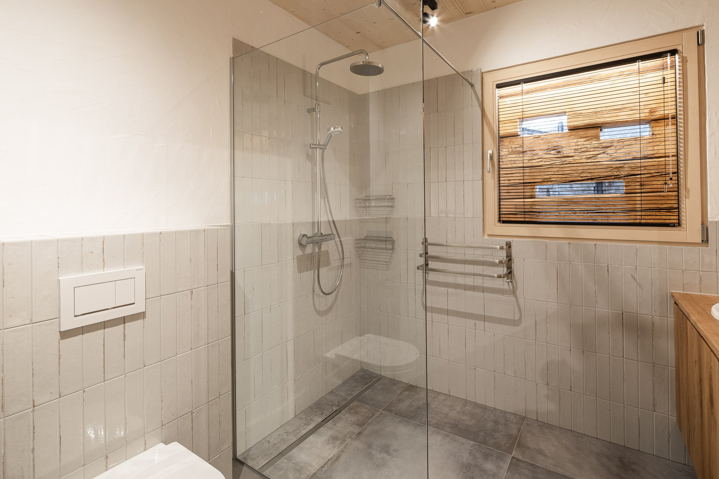 Ein Badezimmer mit Dusche, Wandfliesen, Fenster mit Holzjalousien und einem Handtuchhalter.