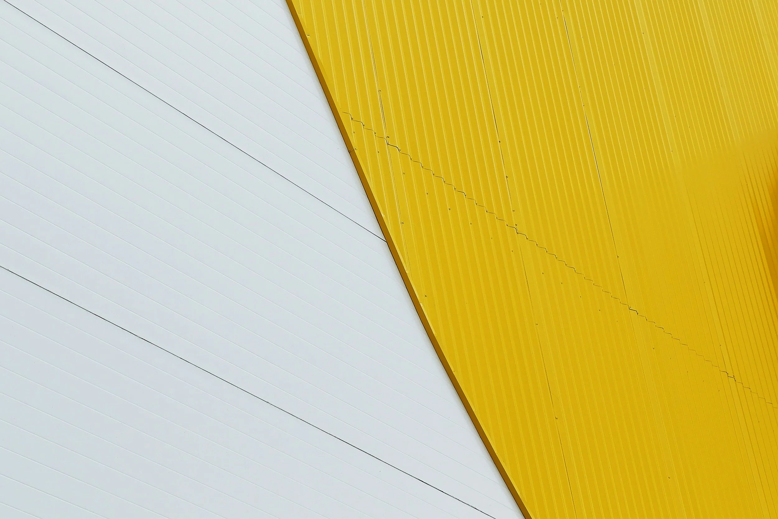 Close-up of a building with white and yellow metal siding, divided diagonally.