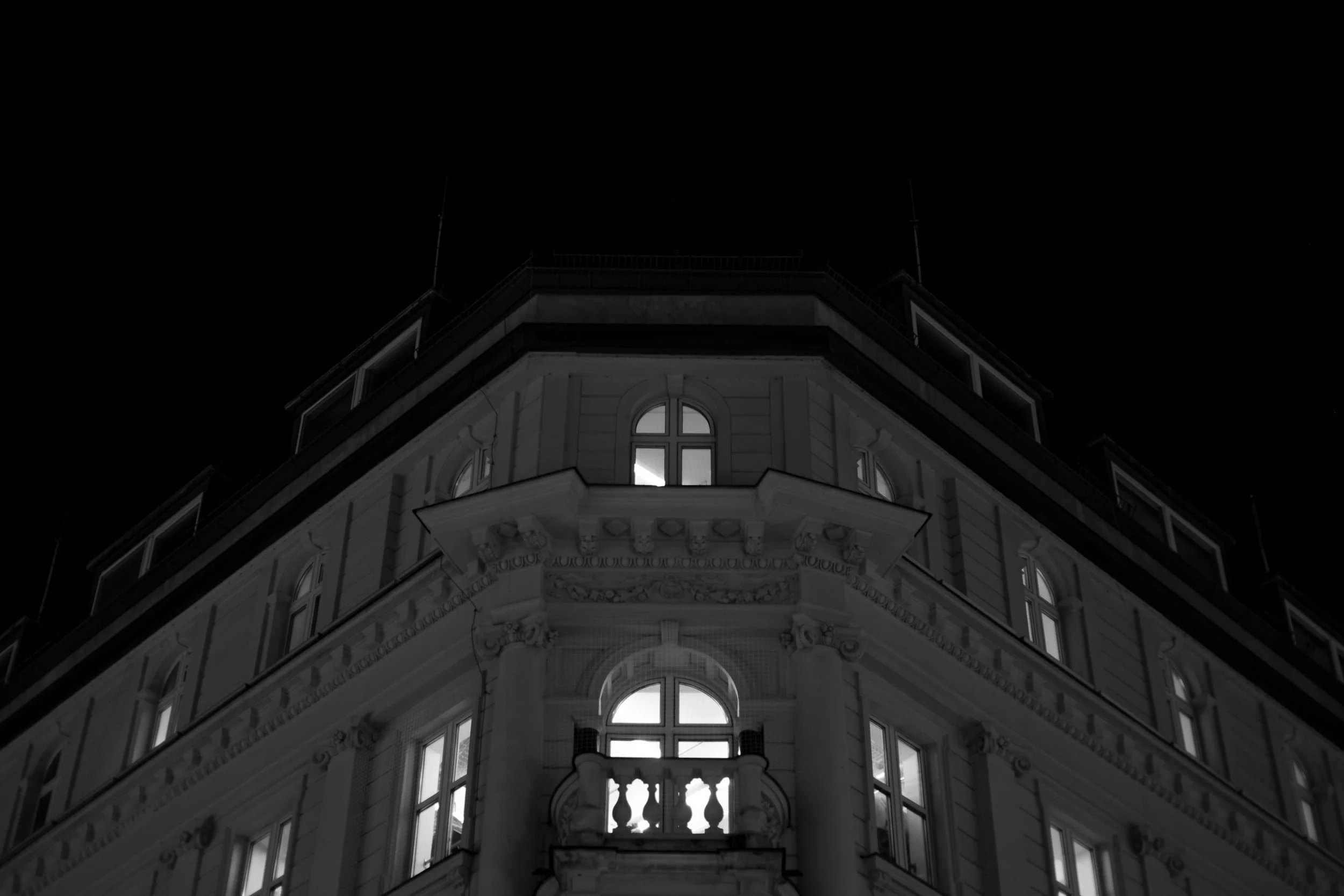 A tall, ornate building at night with illuminated windows and decorative architectural details, viewed from below.