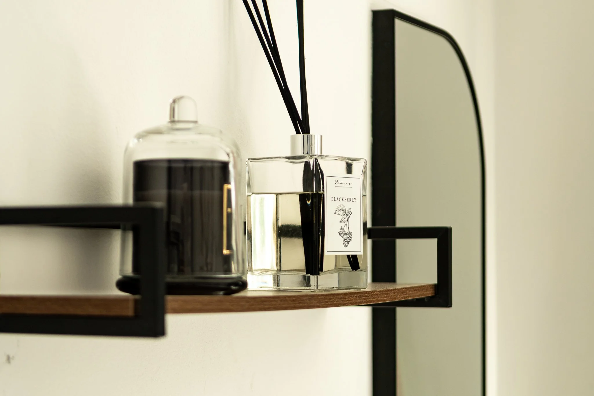 Close-up of a wooden shelf with black metal brackets holding bottles of perfume or scented oils, one of which is labeled blackberry.