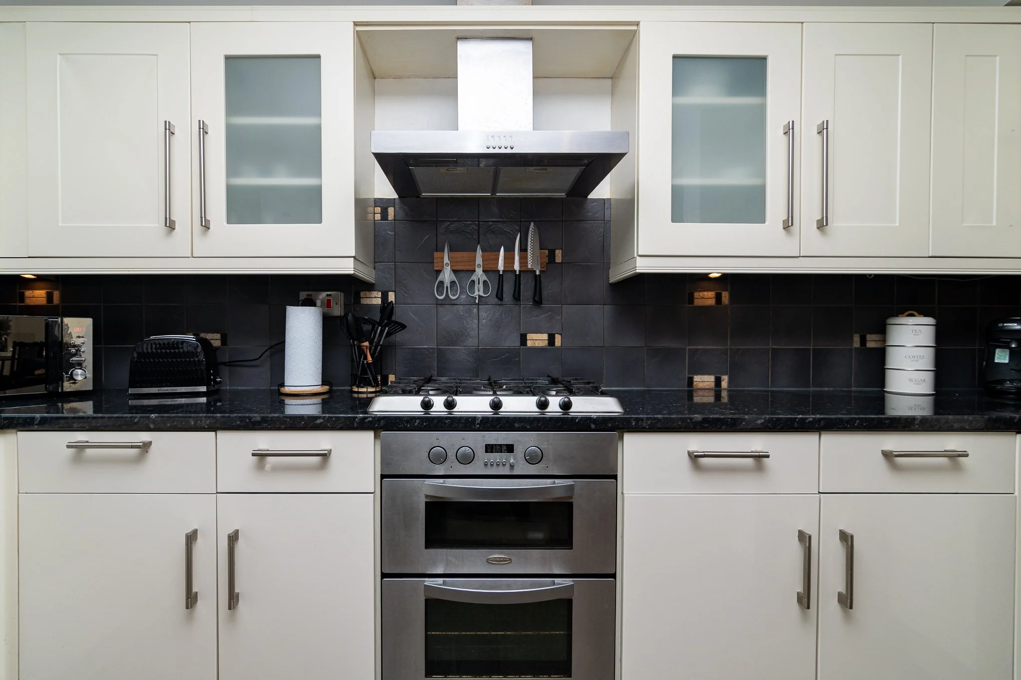 Kitchen with white cabinets, stainless steel stove, black countertops, and hanging knives above the stove.