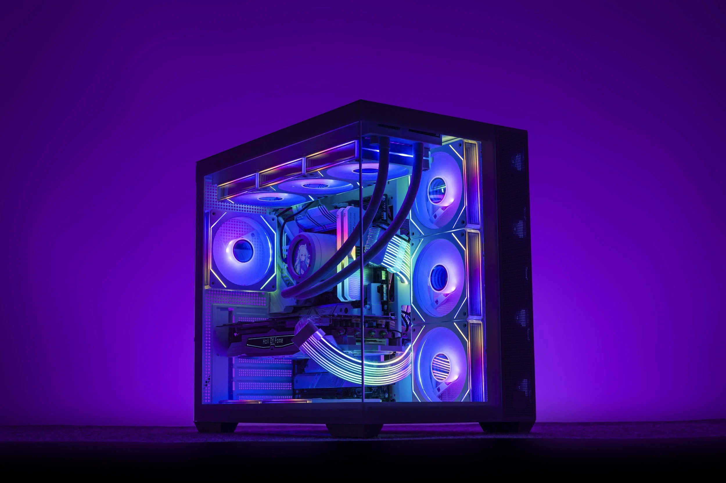 A custom desktop computer with rainbow-colored RGB lighting visible inside a glass case, against a dark purple background.