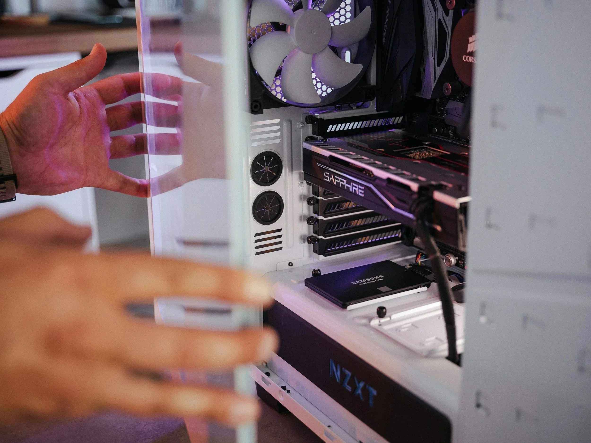 A person's hand opening a computer case, revealing an internal cooling fan and various components inside a white computer case.