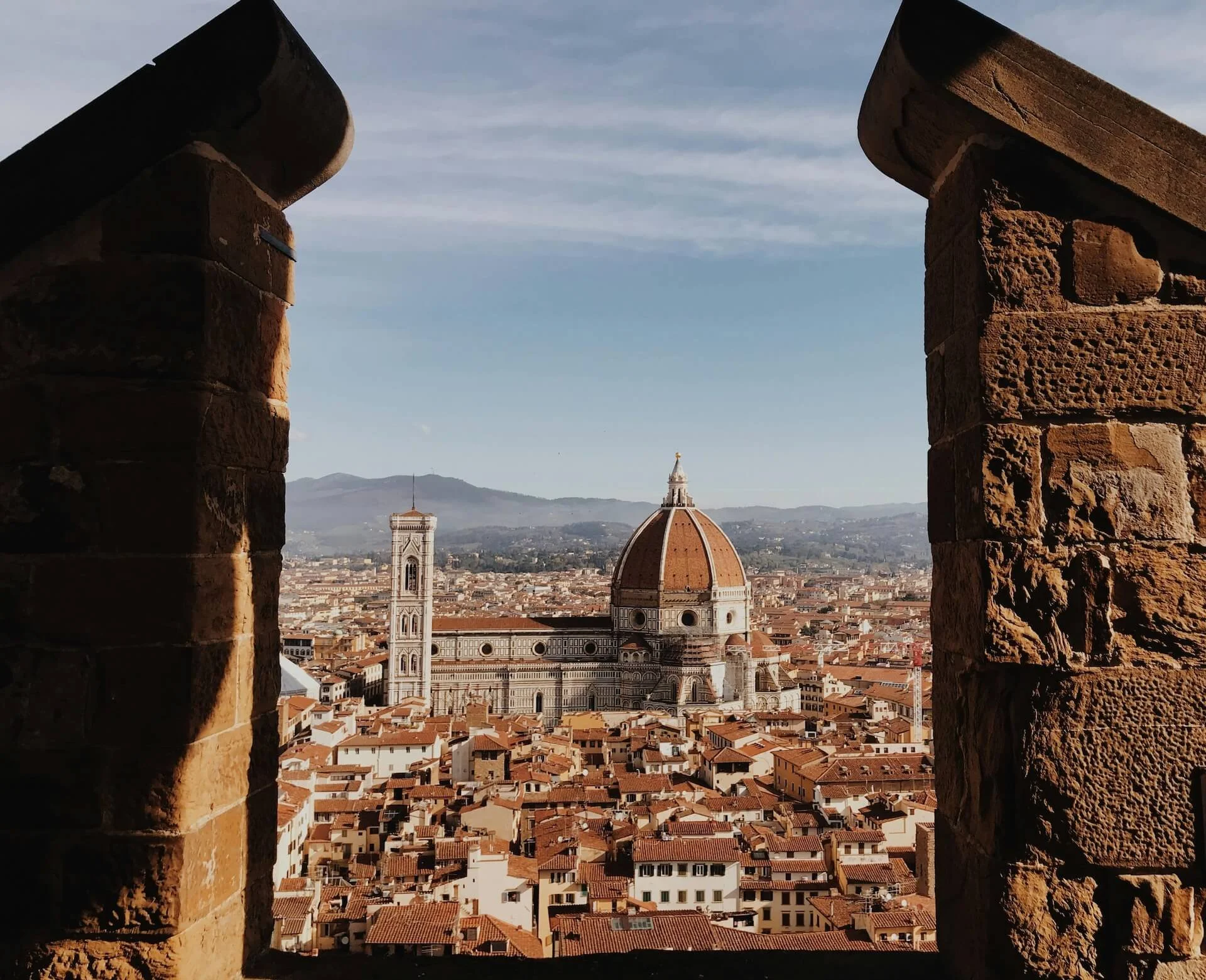 View of a City Centre, Italy seen through a castle window, with a Cathedral  prominently in the center, including its iconic dome, and other historic buildings in the cityscape.