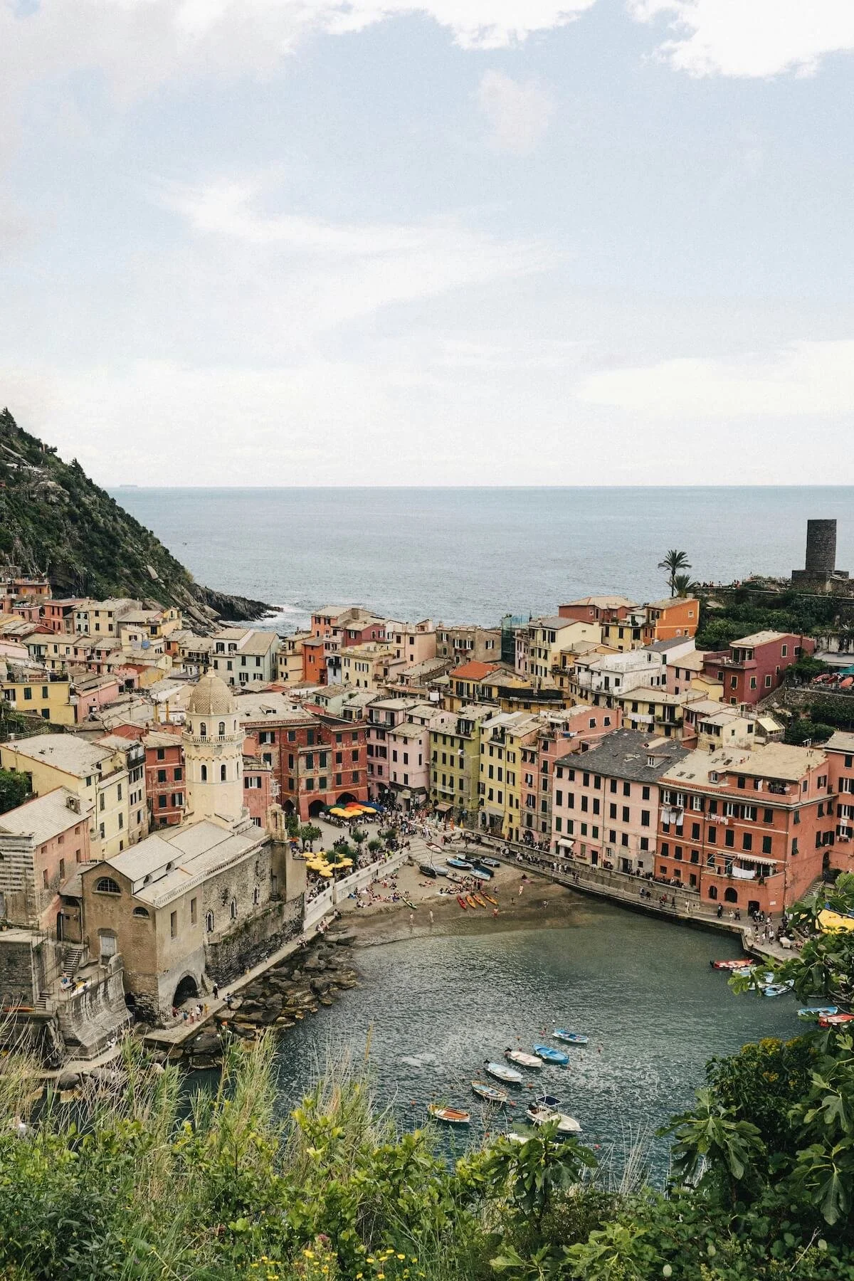 Colourful  village with pastel buildings, a church, and a small harbor with boats, situated along the cliffs overlooking the sea under a partly cloudy sky.