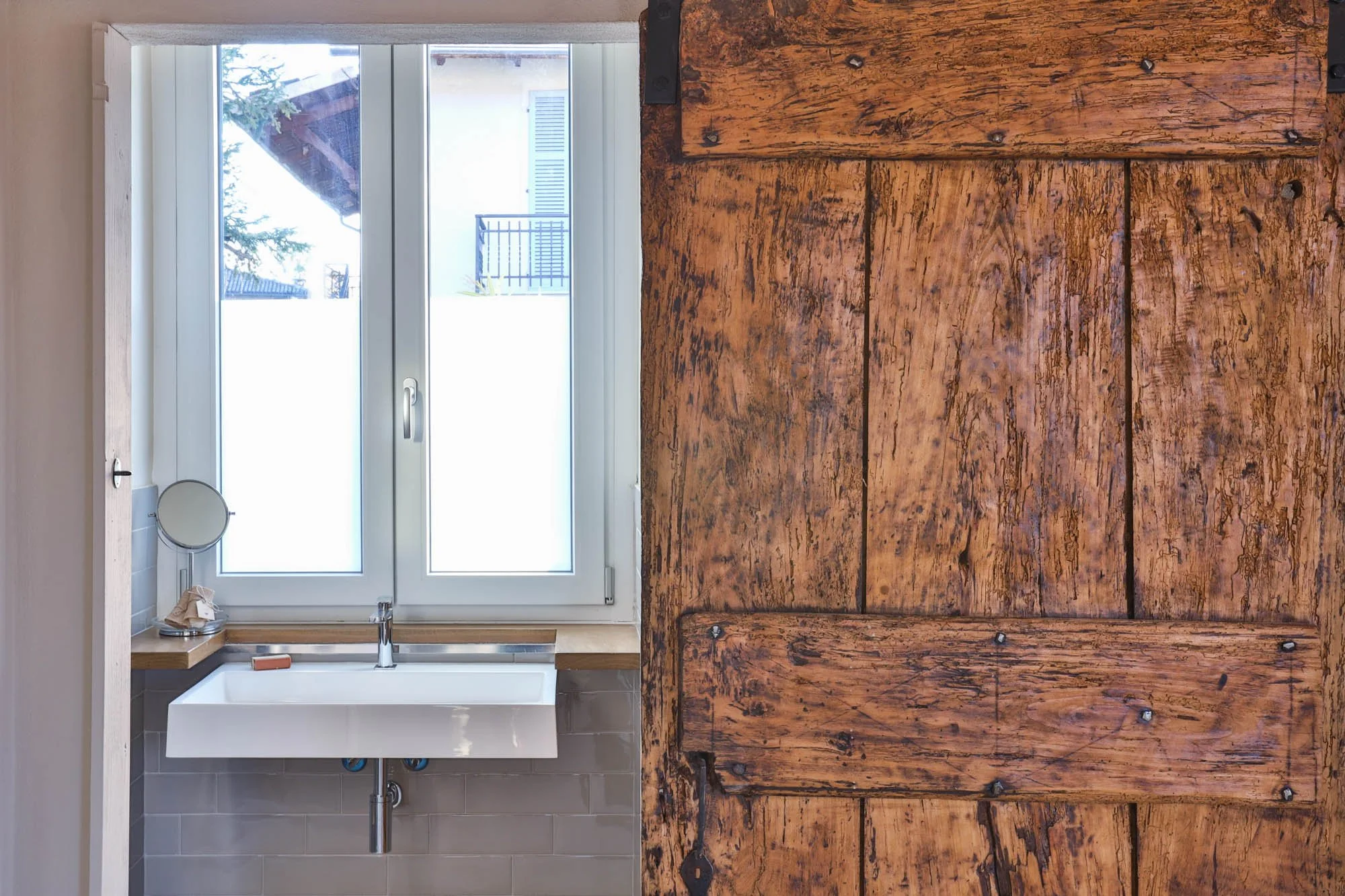Interior view of a kitchen with a white window, white sink, faucet, and a brown rustic wooden countertop.