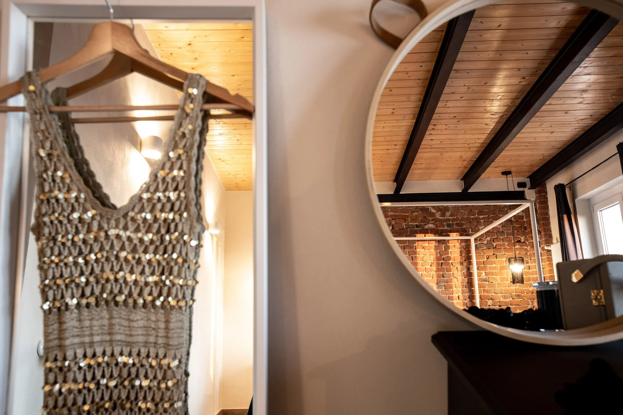 A close-up of a mirror reflecting a room with a wooden ceiling with exposed beams, a brick wall, and a hanging light fixture.
