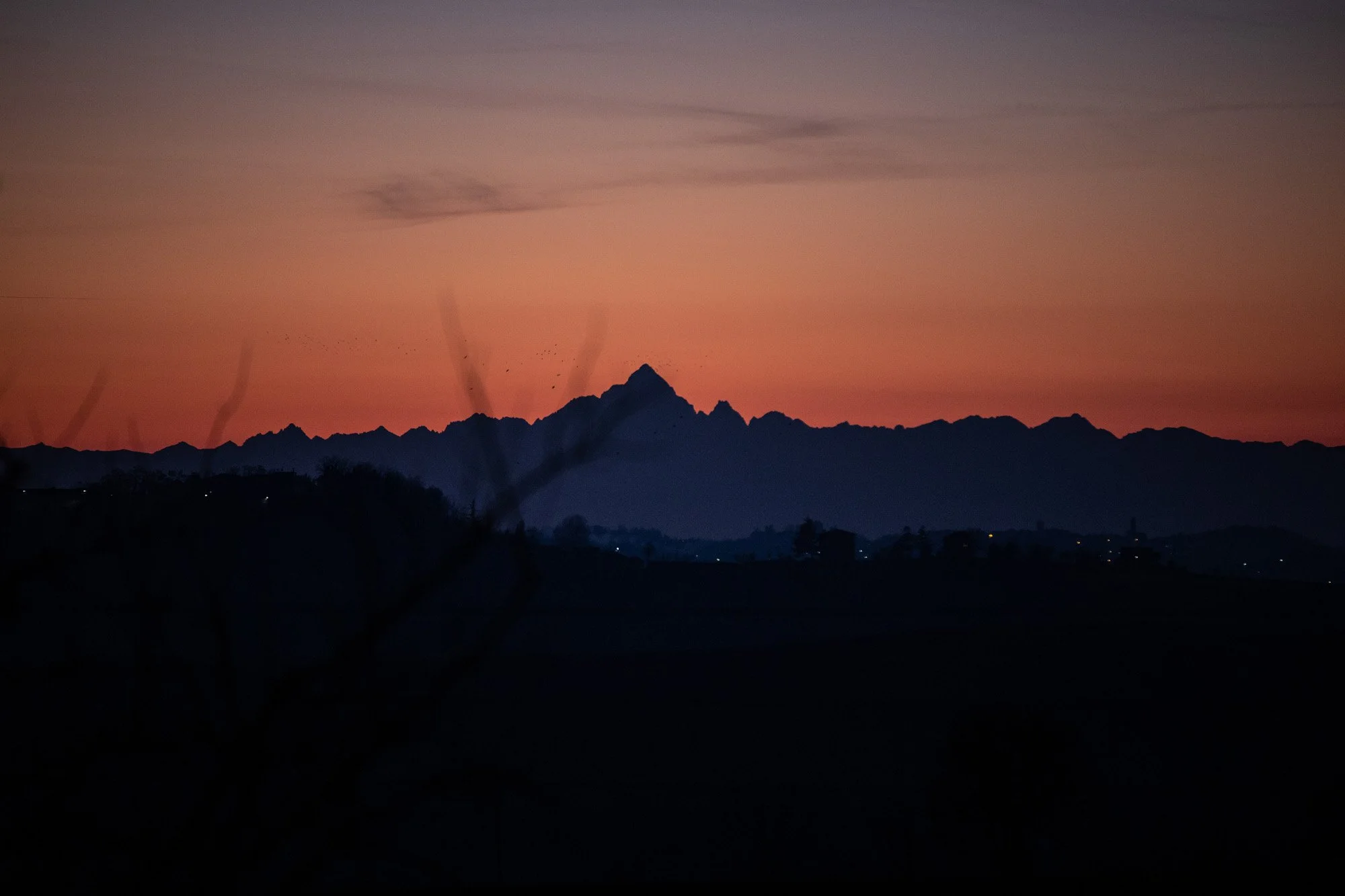 A mountain called Mont Viso at sunset with a pinkish-orange sky and dark silhouettes of mountains and trees in the foreground seen from the terrace at N°18 Casa di Campagna.