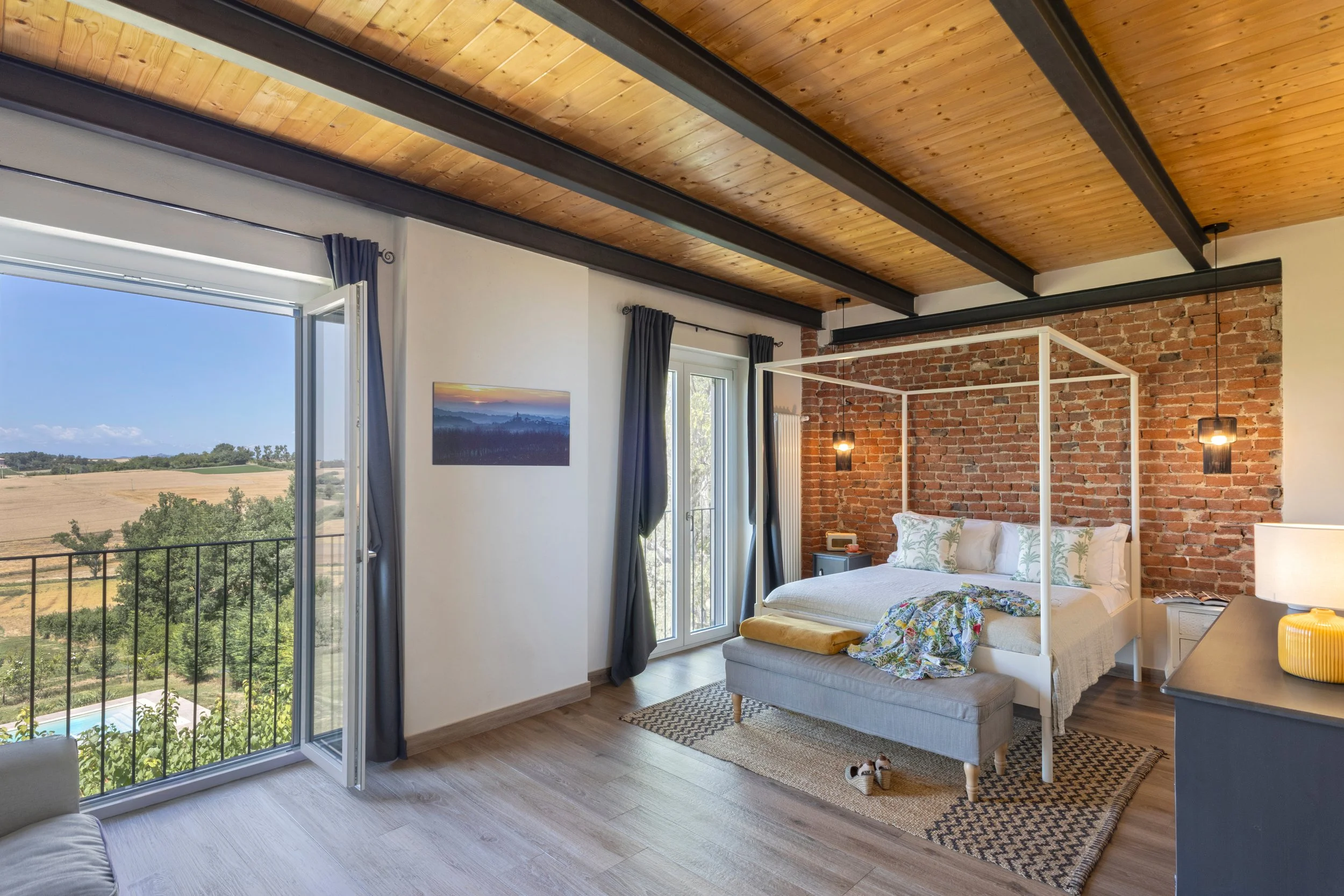 The bright main bedroom with large open windows, a four-poster bed and views on the Monferrato hills and local vineyard.