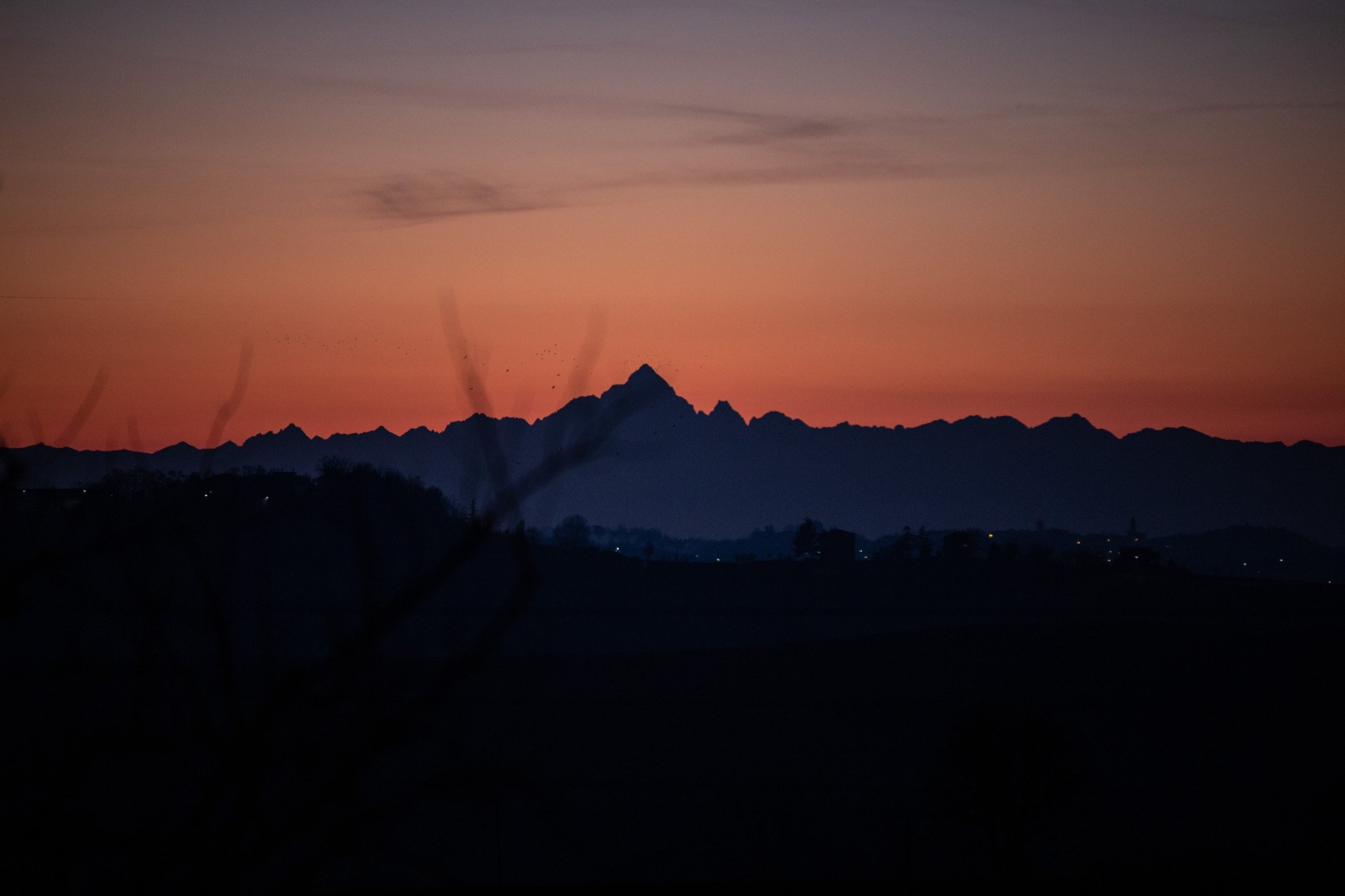Silhouetted mountain range during sunset with pastel pink, orange, and purple hues in the sky and faint clouds.