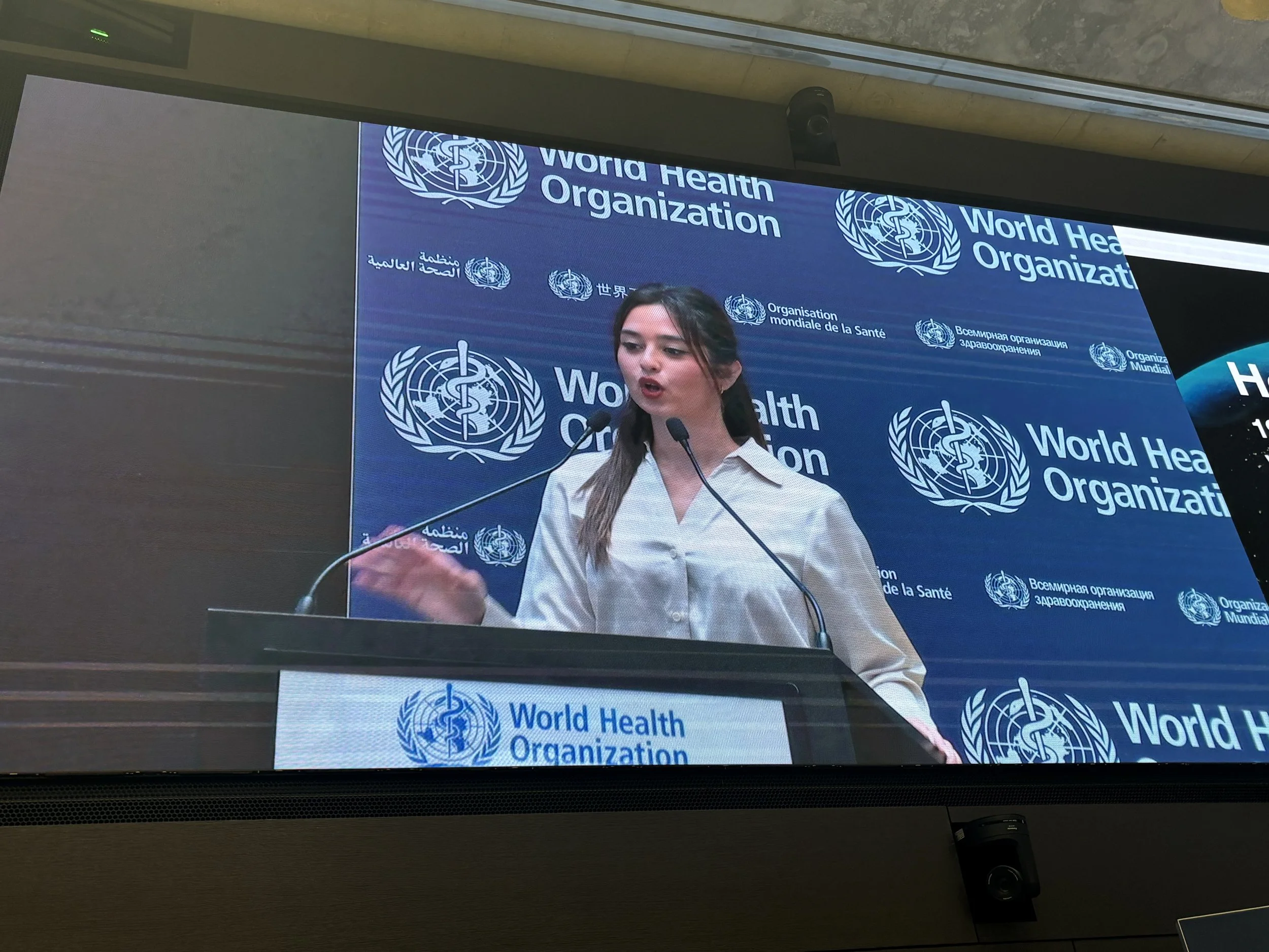 Founder and CEO, Diya speaking at a podium during a World Health Organization event, with a blue background displaying the WHO logo and text in multiple languages.