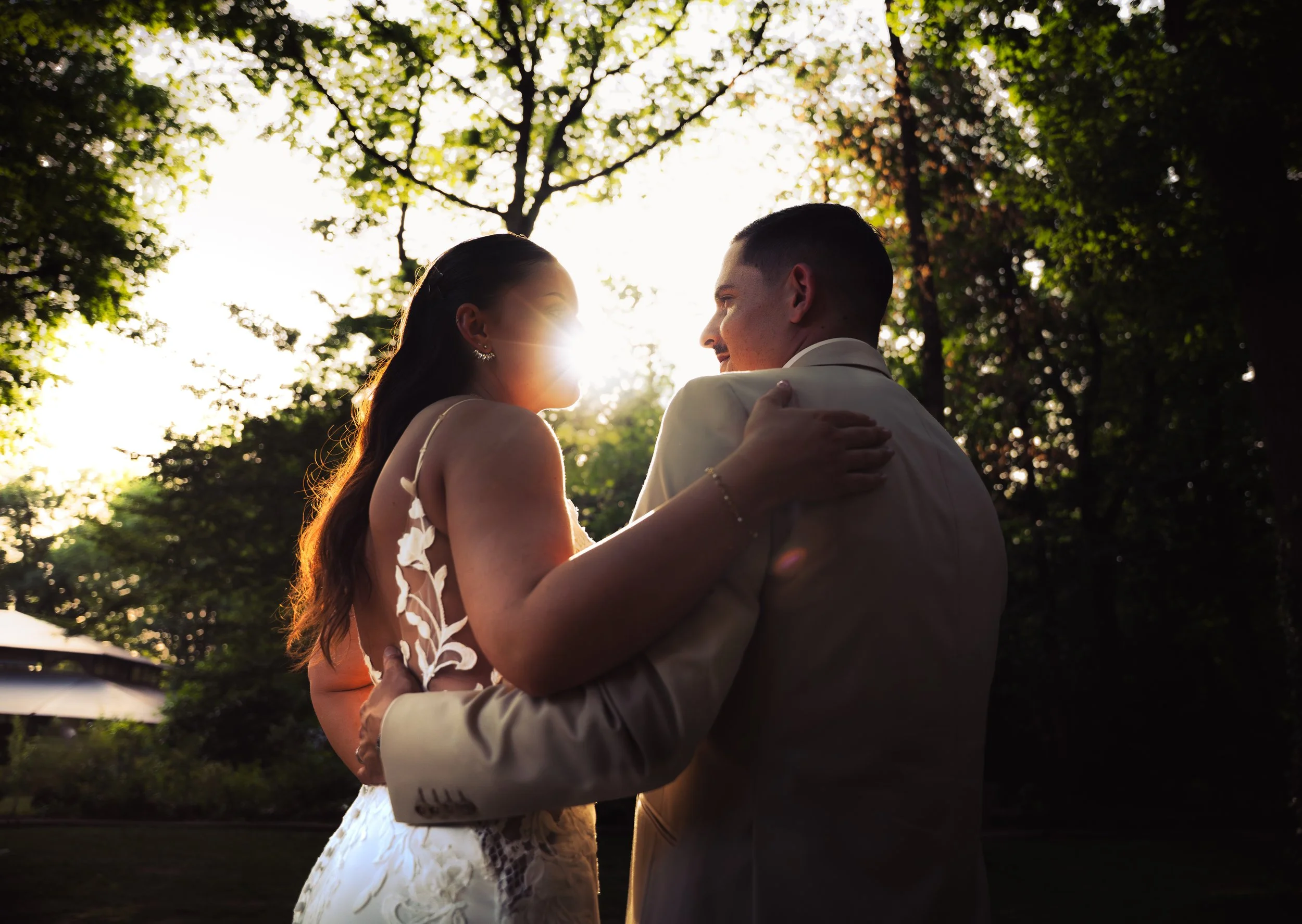 A couple sharing a kiss outdoors during sunset with trees in the background.