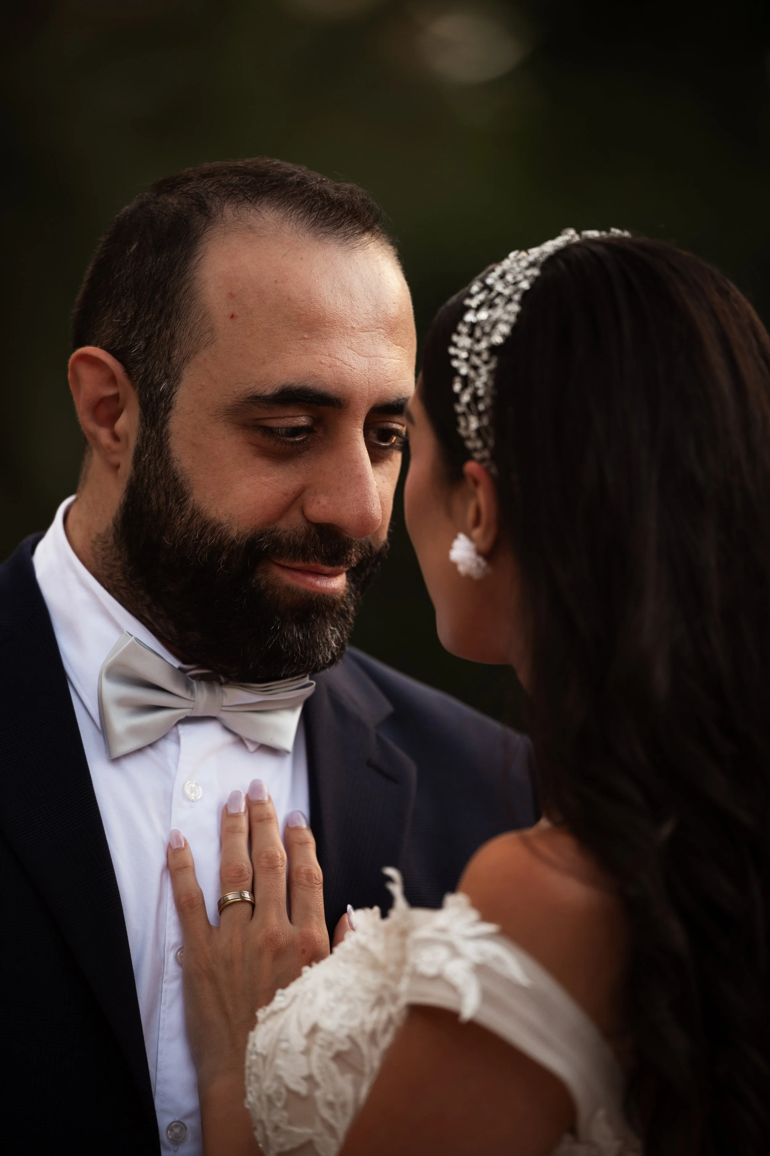 Pareja en boda tocándose las frentes y acercándose, el hombre lleva smoking y la mujer vestido con vestido de novia y accesorio en el cabello.