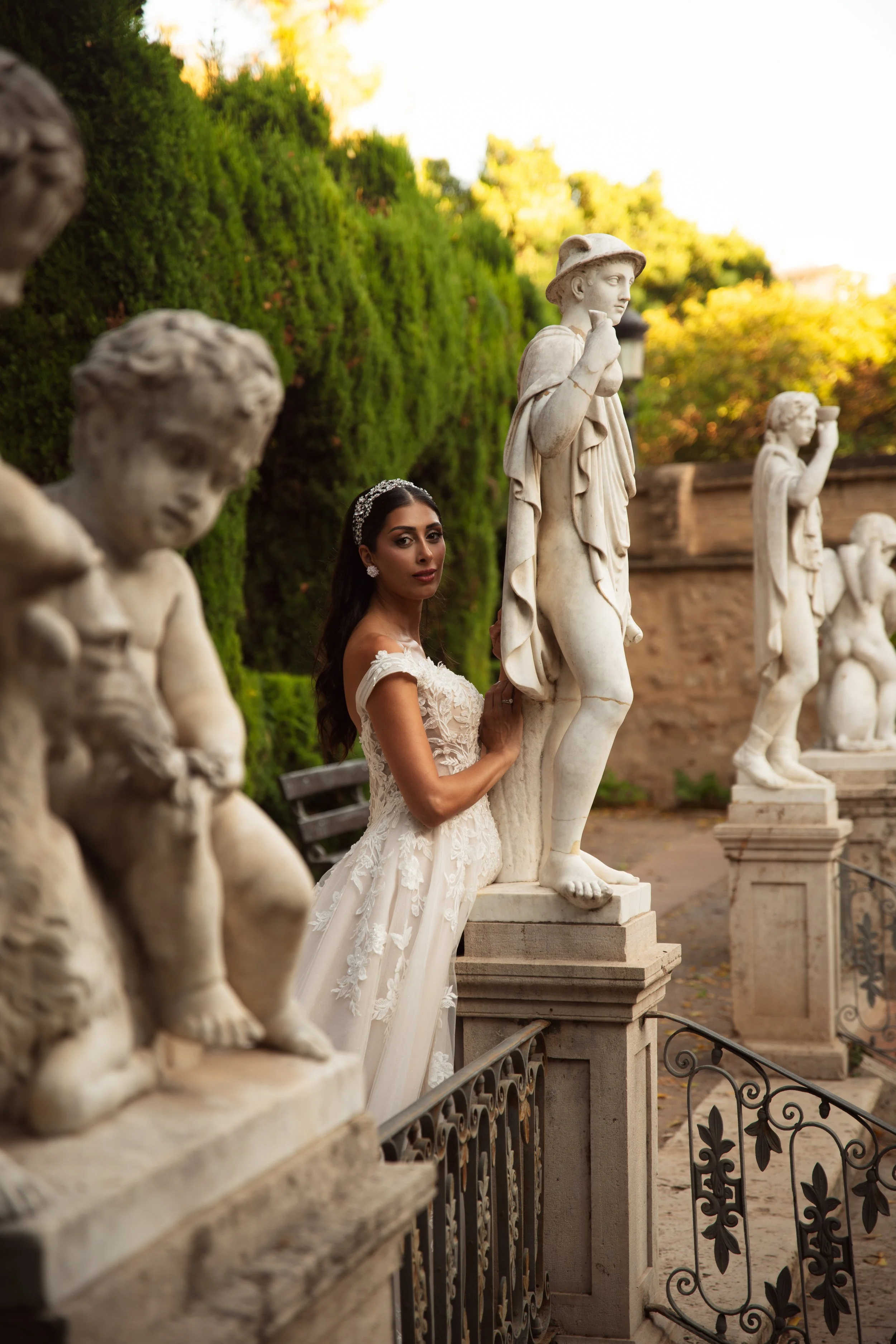 Una mujer con vestido de novia descansando junto a estatuas antiguas en un jardín en otoño