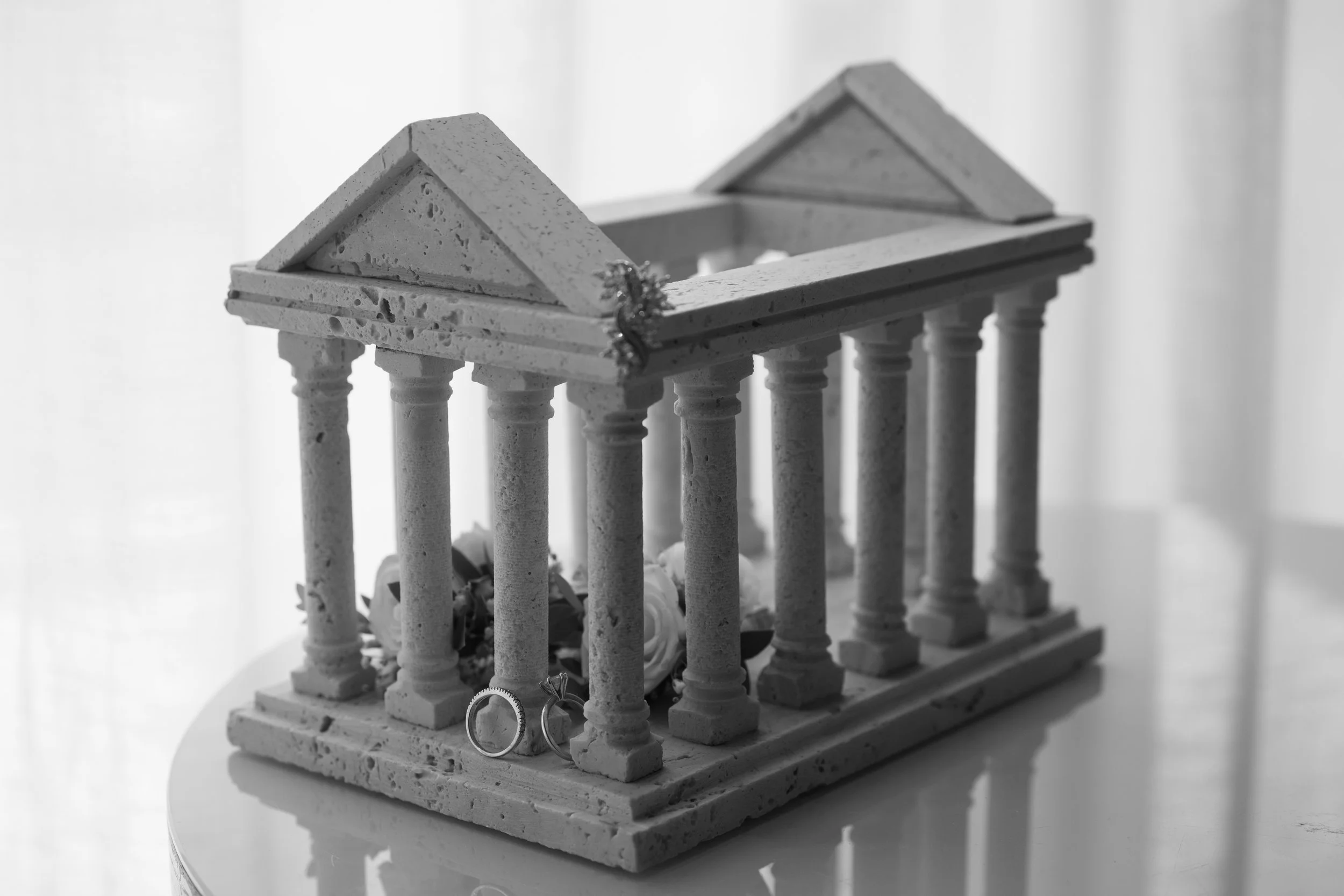 Modelo de un edificio con columnas y techos inclinados de estructura de bloques y columnas, decorado con anillos de boda en la parte frontal.