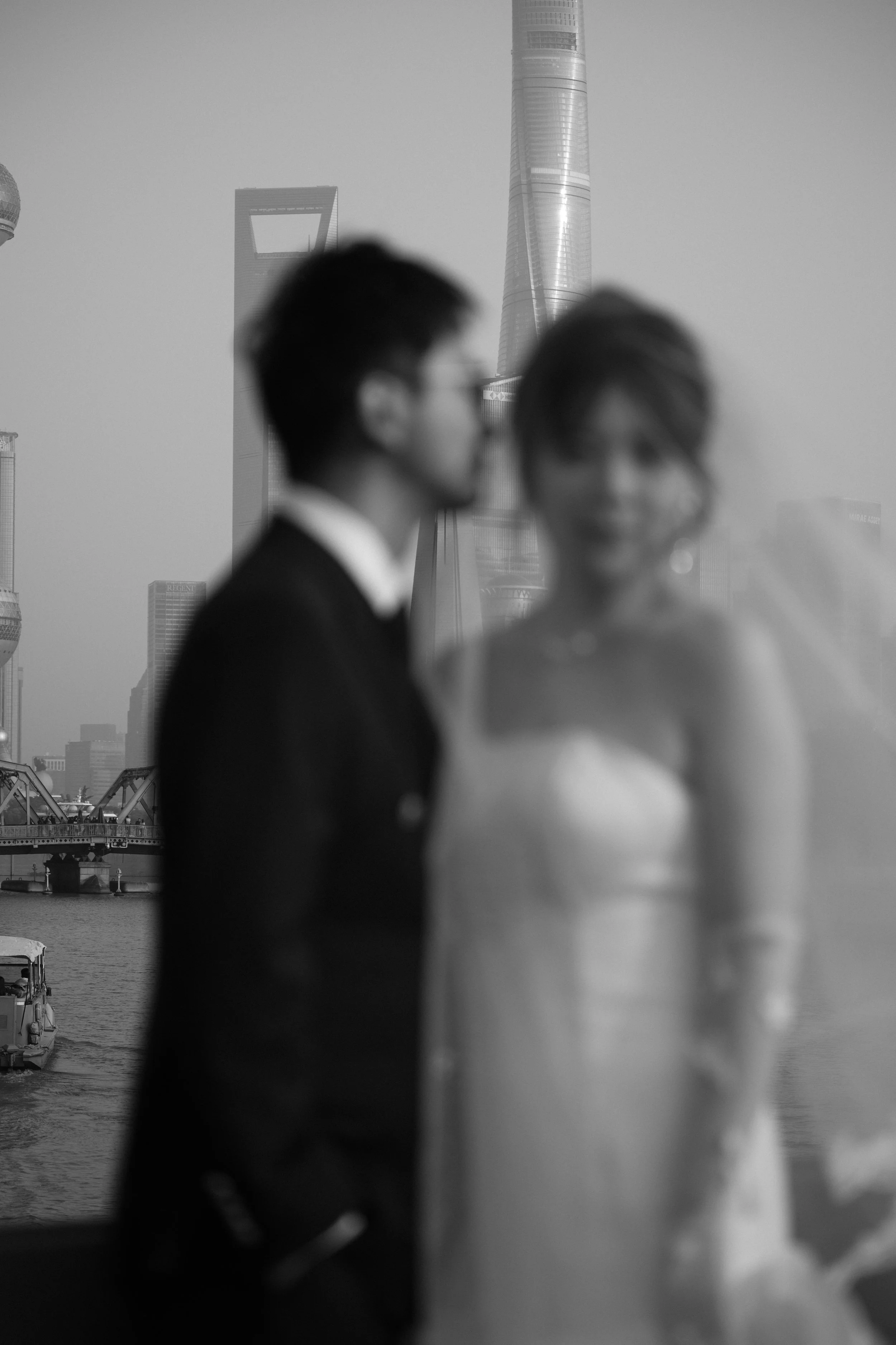 Pareja vestida formalmente en un entorno urbano con rascacielos en el fondo, en blanco y negro.