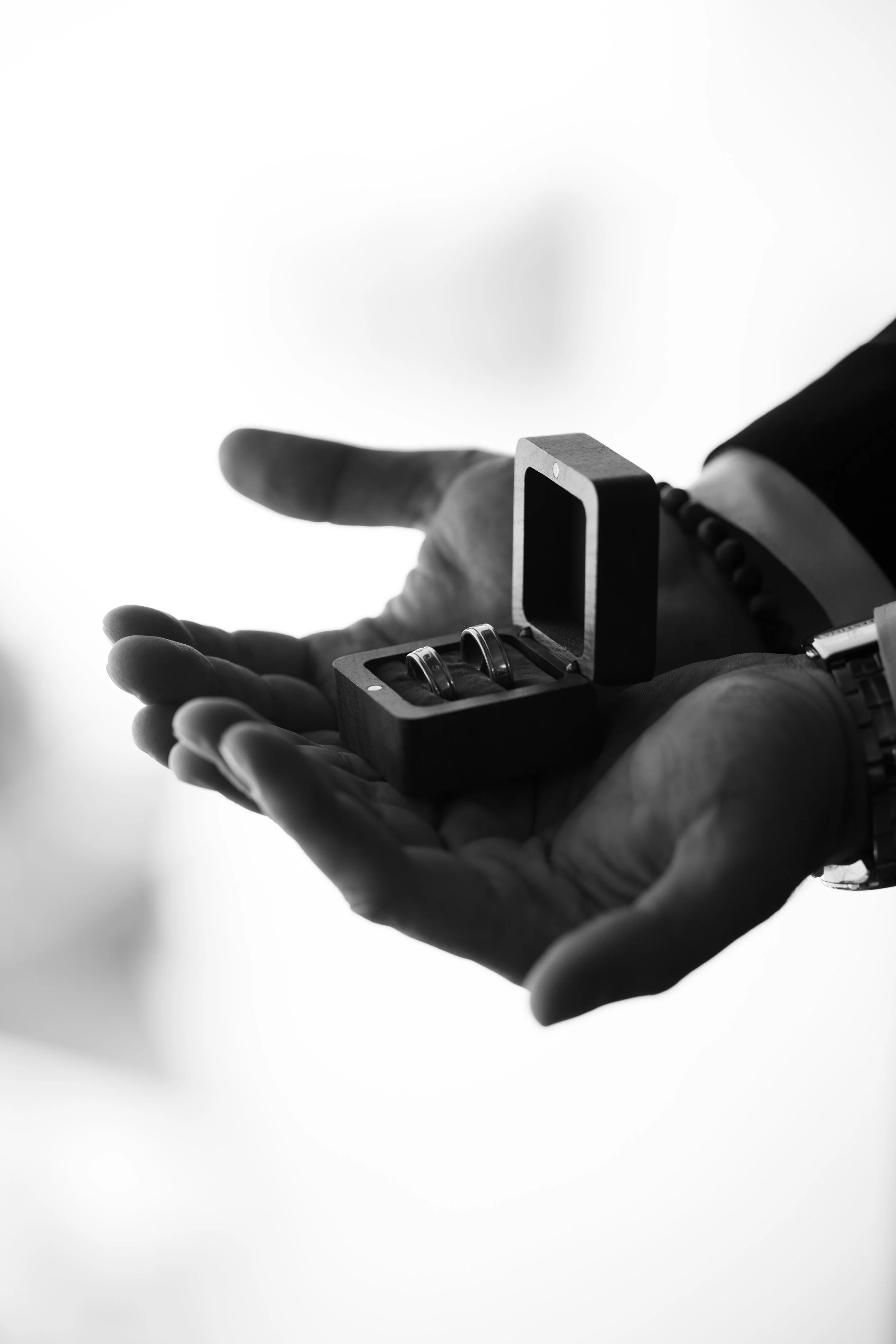 Mano con brazalete y reloj sosteniendo caja con anillos de matrimonio.