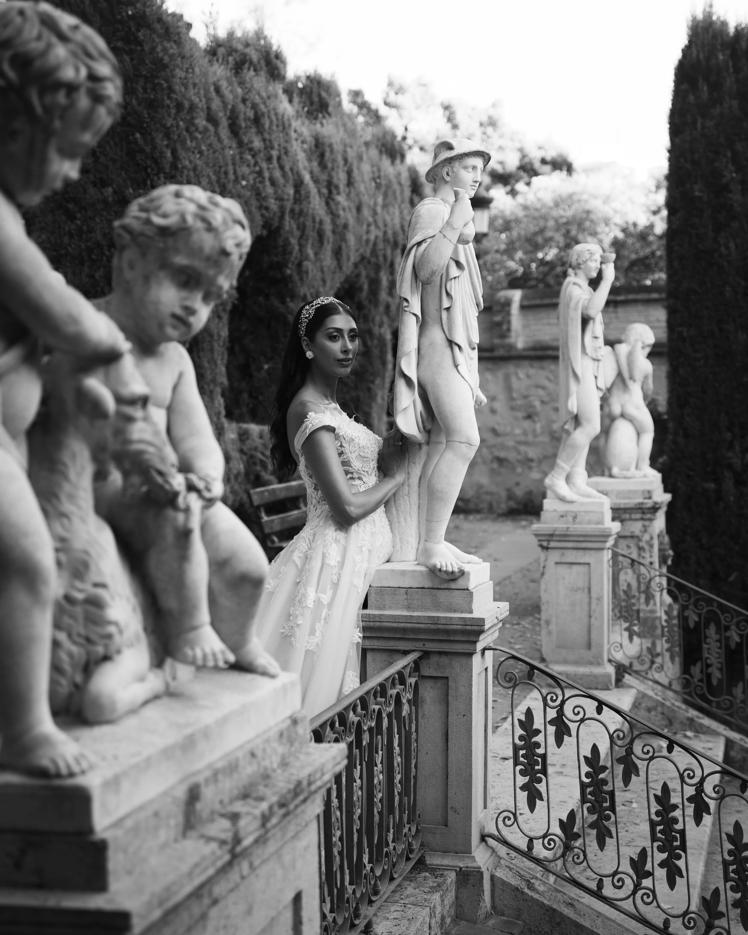 Mujer con vestido de novia entre estatuas de mármol en un jardín, en blanco y negro.