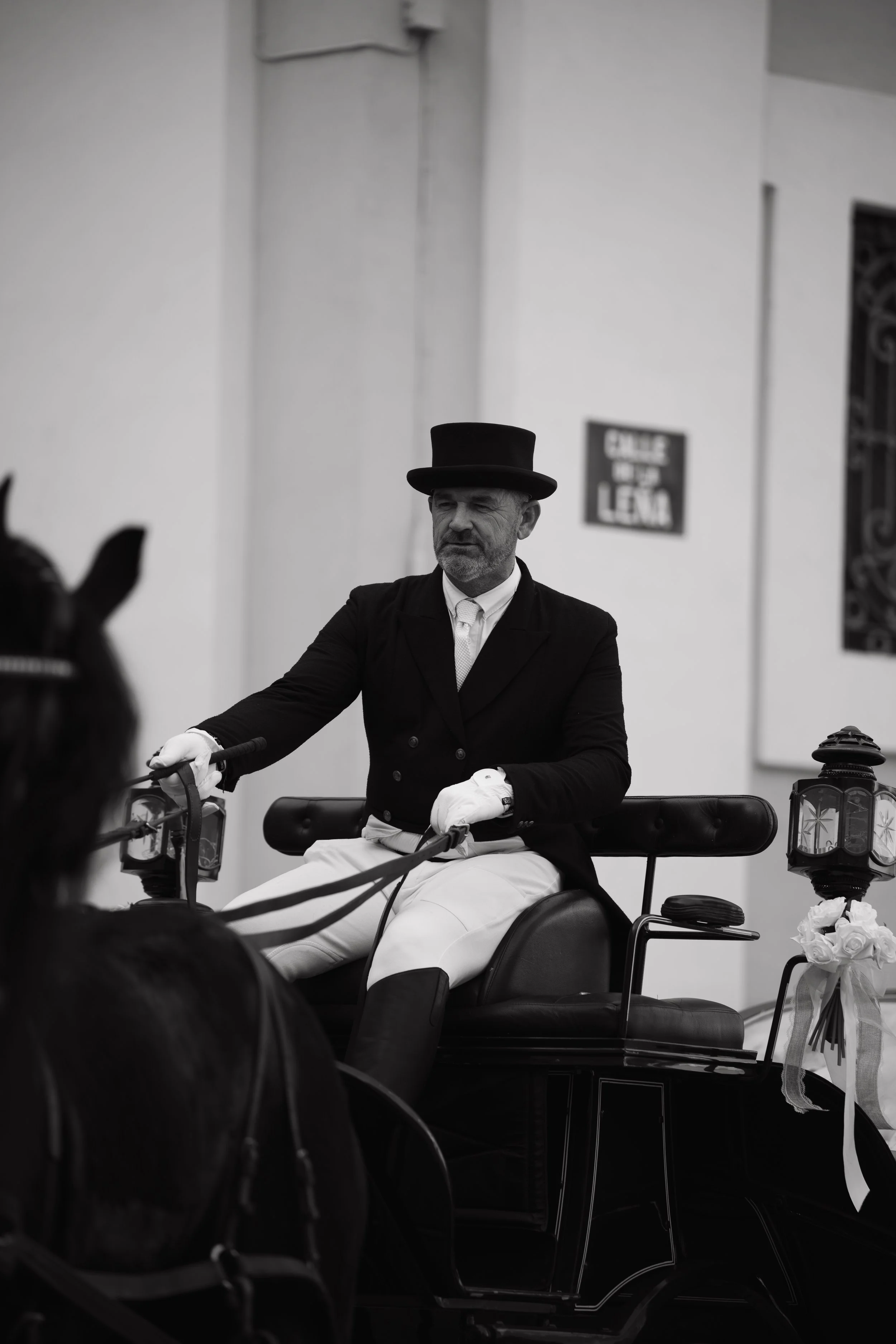 Hombre vestido con uniforme de caballero andante, con sombrero alto, sentado en una carroza decorada con farolas y flores, en un entorno que parece una iglesia o un lugar ceremonial.