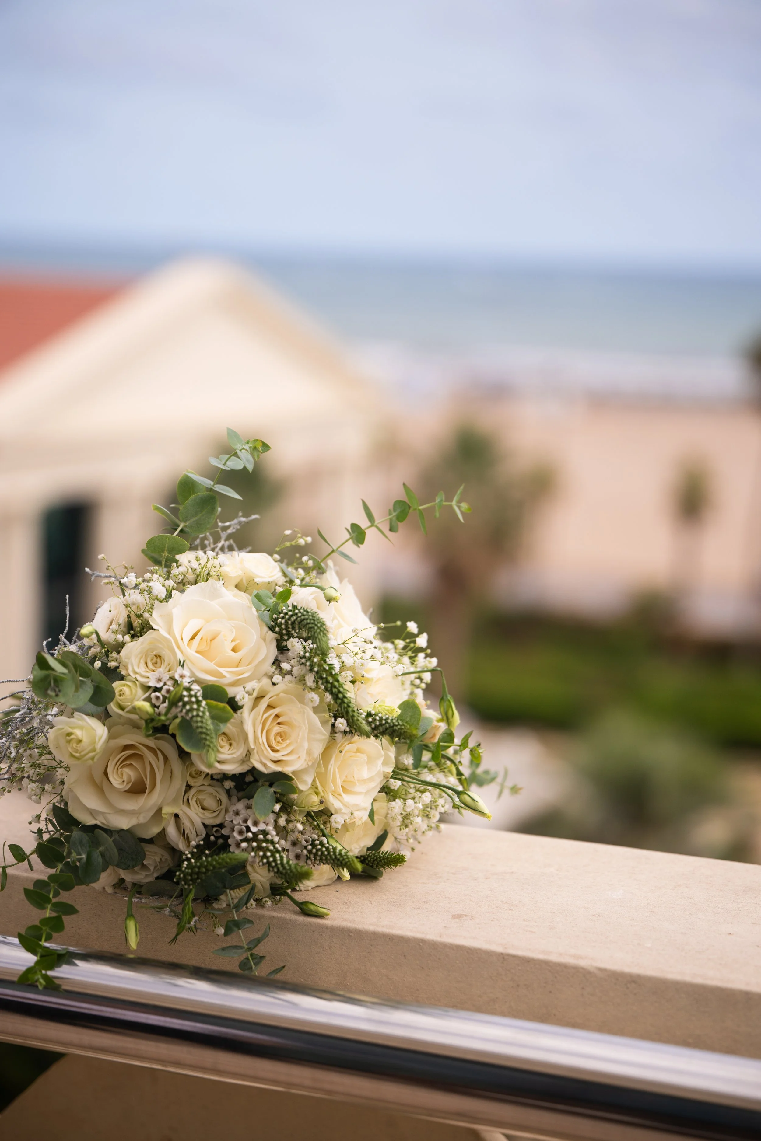 Ramo de flores blancas con rosas y verdes en fondo difuminado de una escena exterior con cielo y edificios.