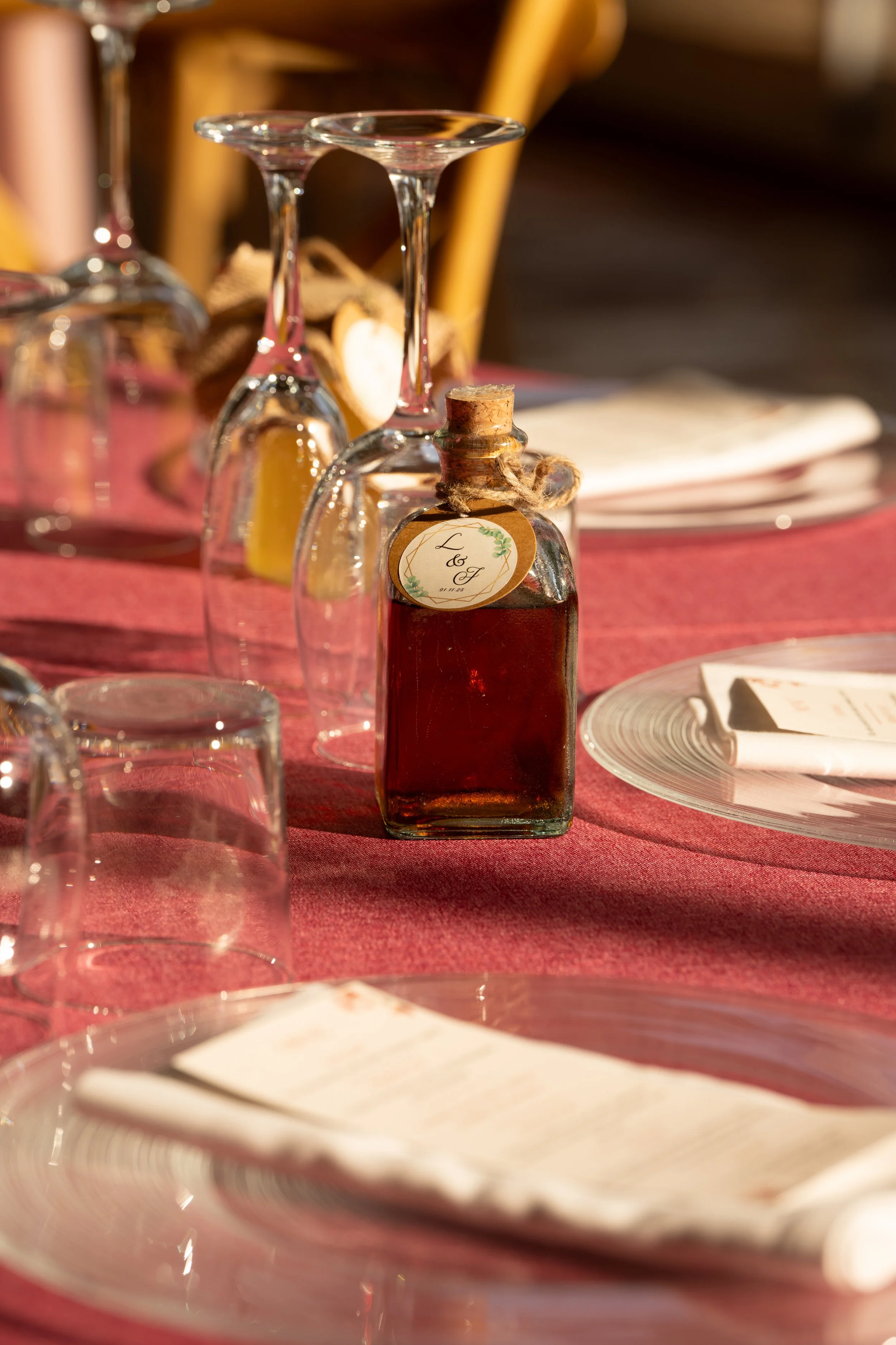 Vasos de cristal con vino tinto en una mesa decorada con mantel rojo y platos blancos, en un ambiente de celebración o comida elegante.