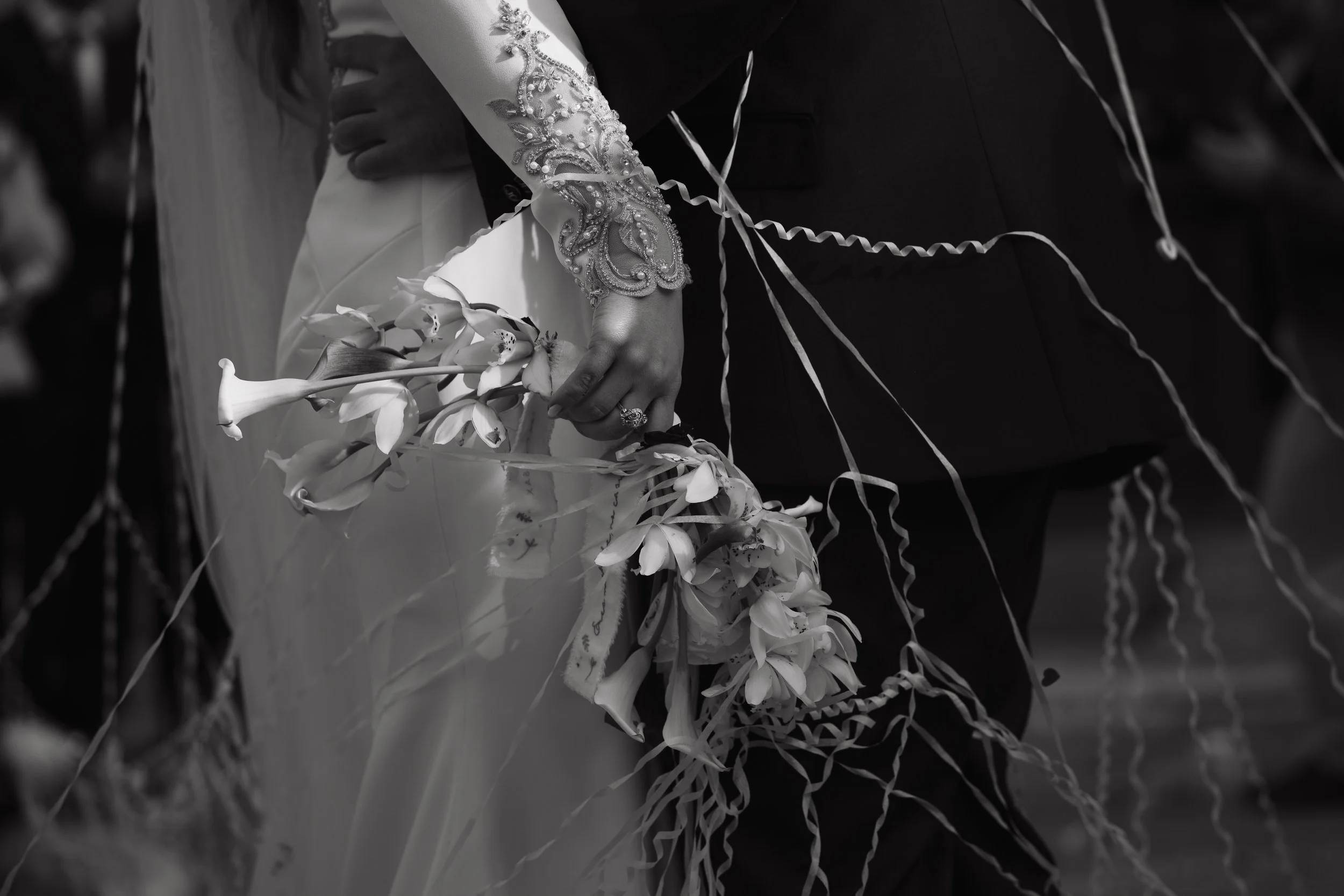 Pareja bailando en su boda, vestido de novia con bordados y bouquet de flores blancas, en un ambiente formal.