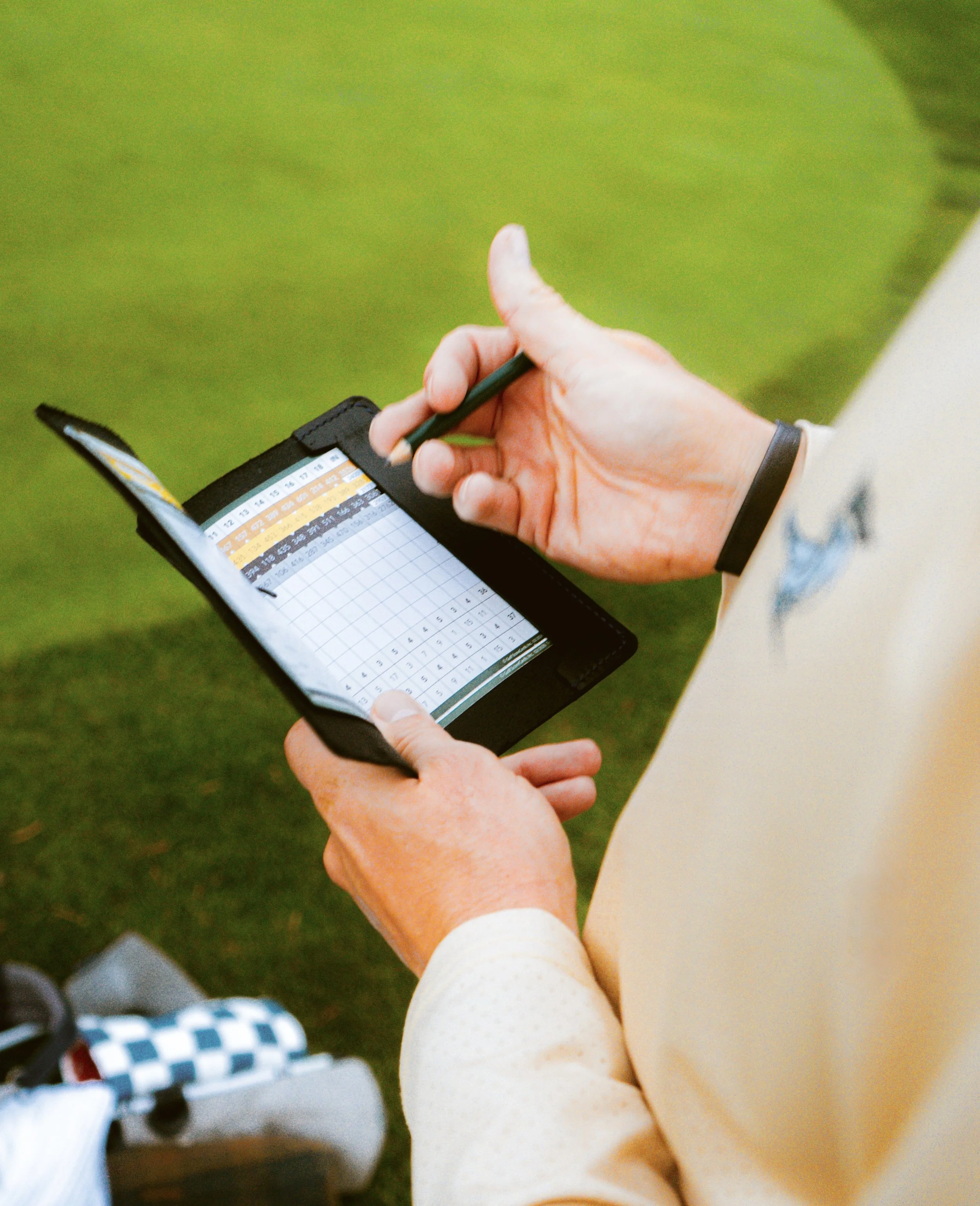 A person holding a golf scorecard and pencil, wearing the Staple Sun Shirt taking down a score.