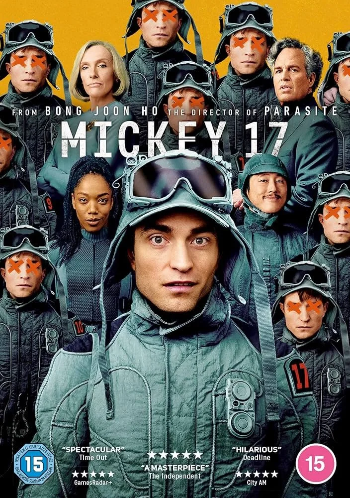 Promotional poster for the movie "Mickey 17" showing a group of actors in dark flight suits and helmets, with some faces marked with orange Xs, and two actors in regular clothing. The poster includes a pink age rating icon, review quotes, and credits