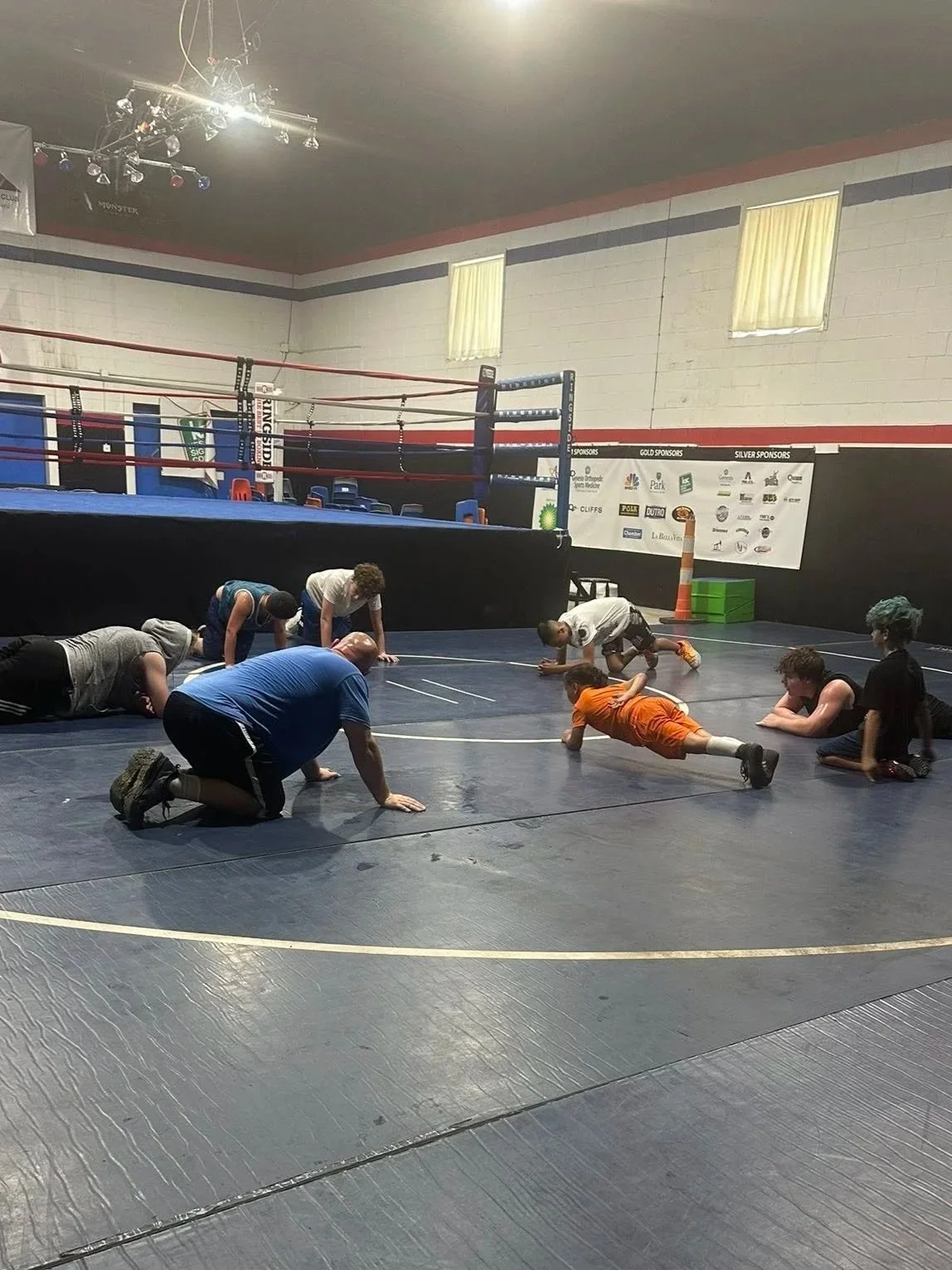 Children and adults in a wrestling gym doing push-ups and exercises on the mat.