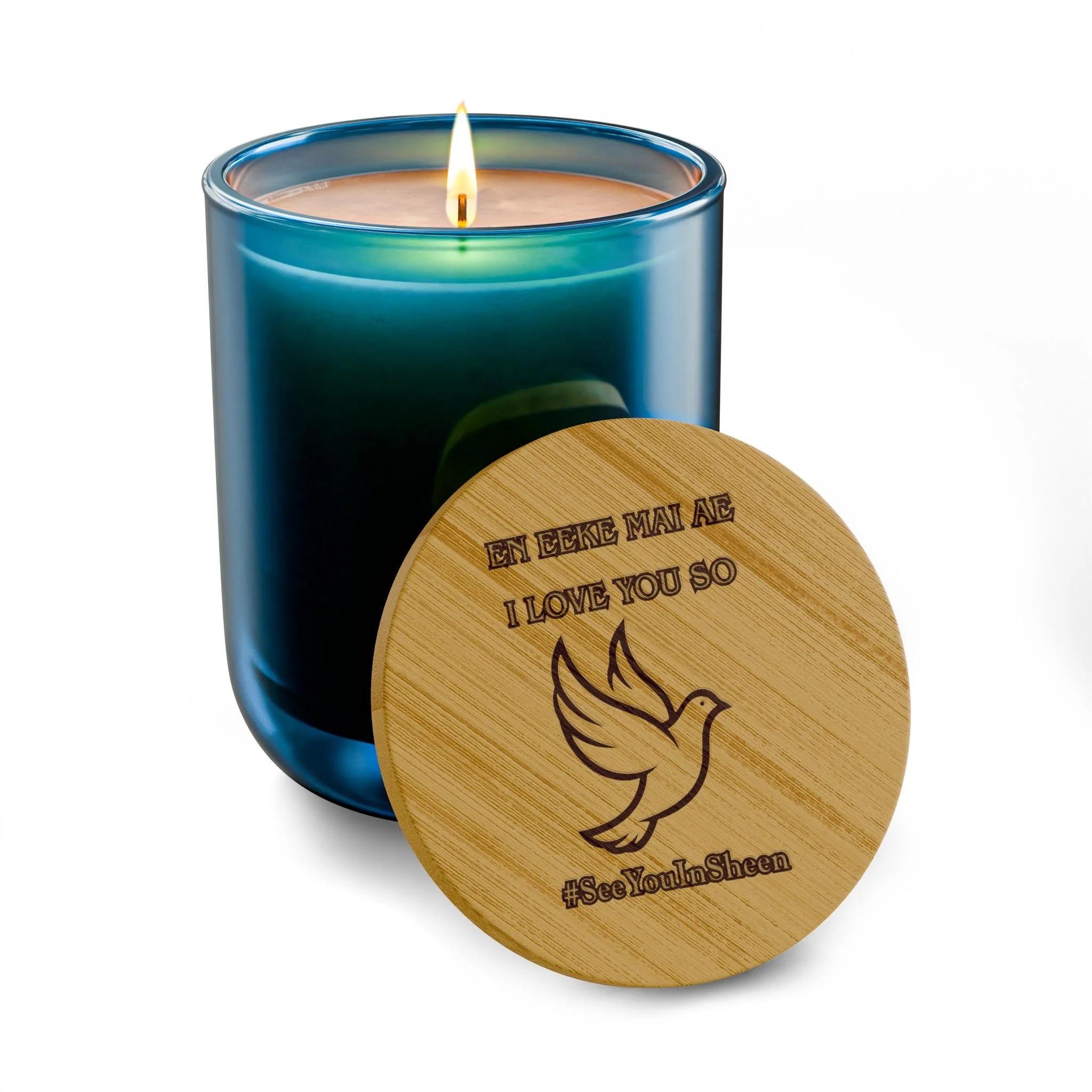 A lit candle in a blue glass holder with a wooden lid that has text and a drawing on it.