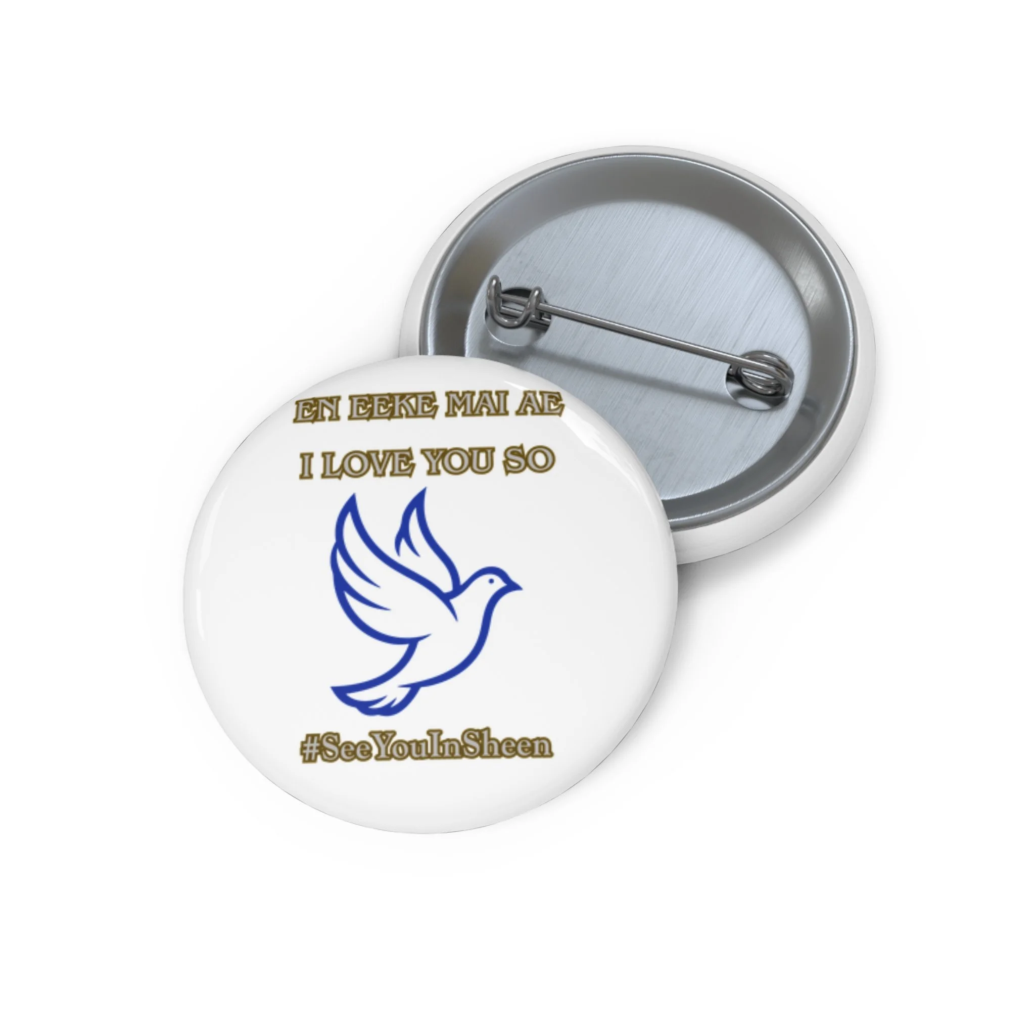 Close-up of a white mug with a blue dove design and the words 'EN EKE MA AE I LOVE YOU SO' in gold lettering, lying on its side with the inside visible, a metal spoon resting inside the mug, and a partial view of a second mug with hashtags '#SeeYouIn