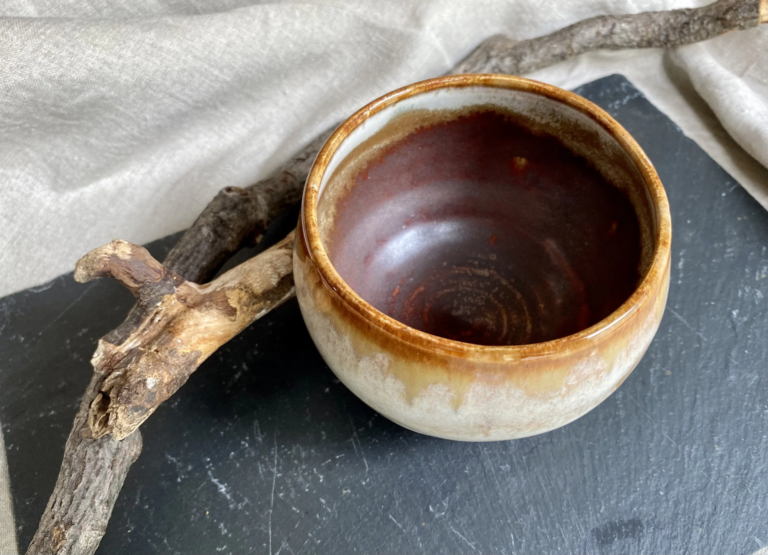 A hand built ceramic bowl sitting on a black surface, with a textured fabric and a piece of driftwood nearby.